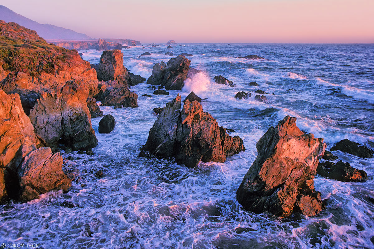 Waves and surf crash among rocks along coast at sunset near Lucia, California