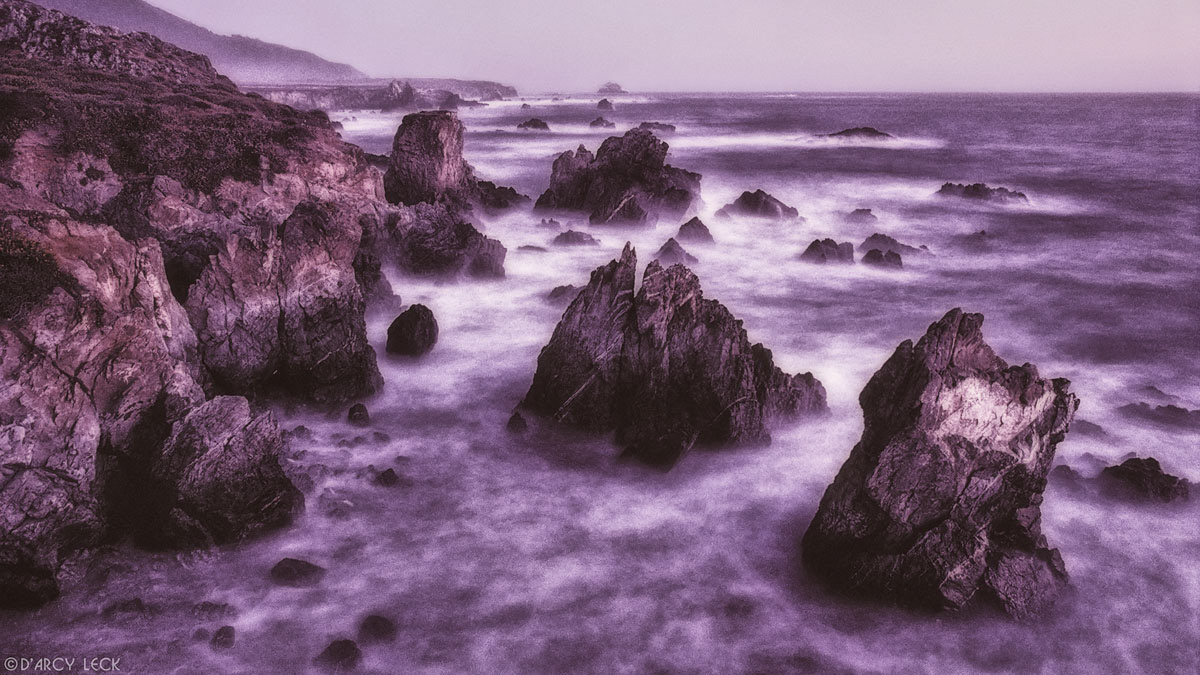 Surf mingles among large rocks at dusk near Lucia, California