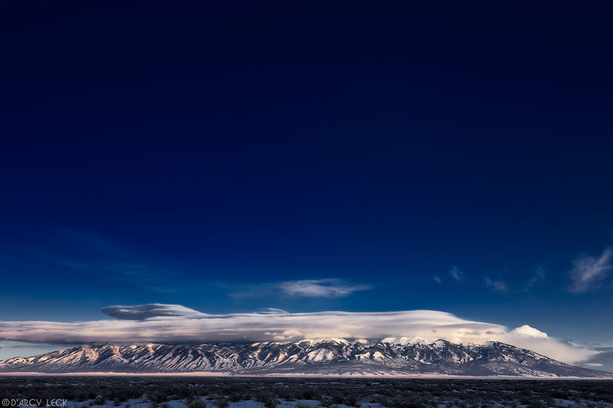 Lenticular clouds cap the snowy Blanca Peak and the Sangre de Cristo Mountains as they rise above the San Luis Valley in winter, Colorado