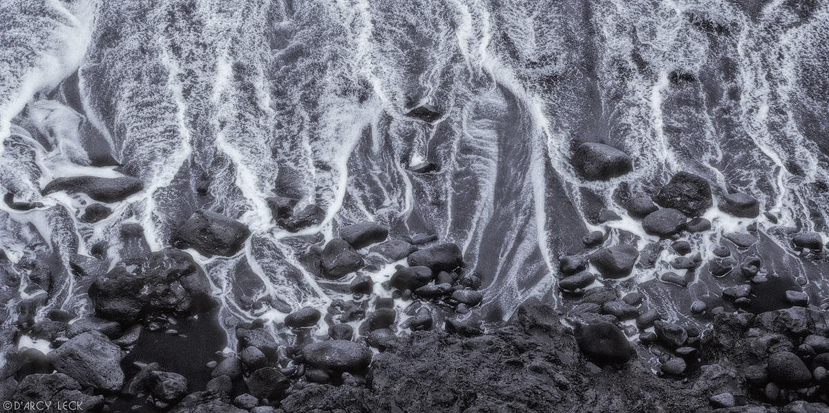 Receding surf leaves trails of water among lava rocks and down black sand beach on the big island of Hawaii