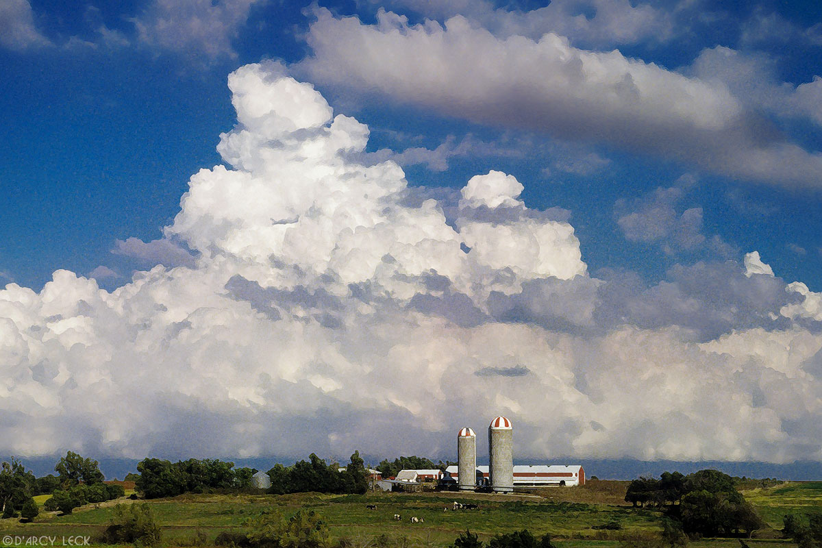 Farm with grain elevators, swelling cumulonimbus clouds growing into thunderstorms in northeastern Kansas