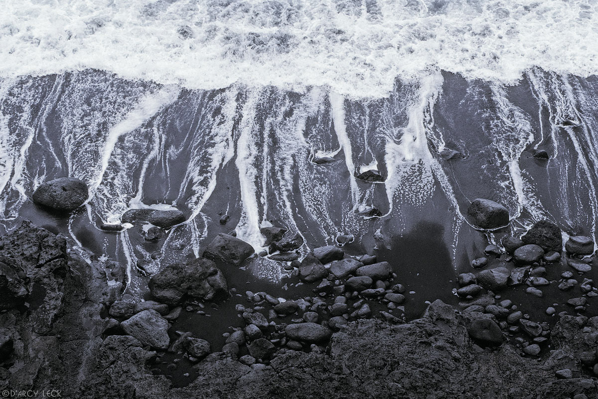 Receding surf leaves trails of water among lava rocks and down black sand beach on the big island of Hawaii