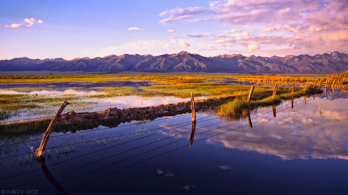 Flooded range land and barbed-wire fence reflect the Sangre de Cristo Mountains at sunset, Colorado