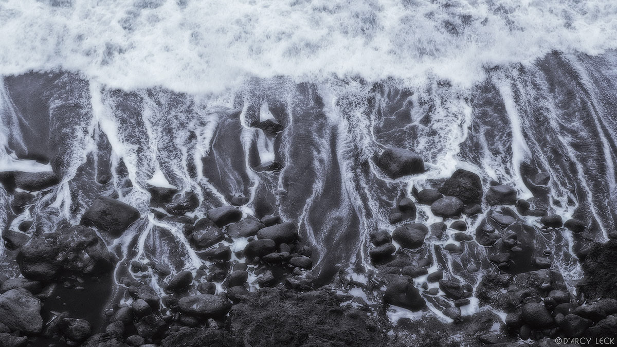 Receding surf leaves trails of water among lava rocks and down black sand beach, big island of Hawaii