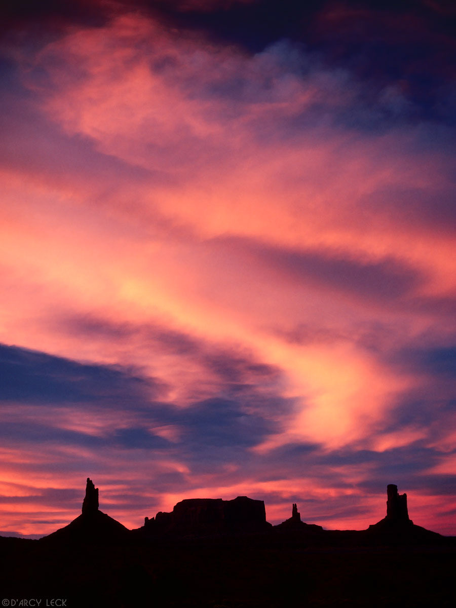 Sandstone buttes silhouetted against sky and clouds illuminated by sunset light, Monument Valley Arizona