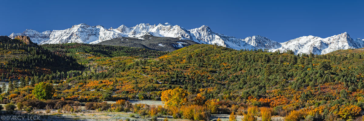 Early Autumn morning light illuminates the snow-capped peaks of the San Juan Mountains in the Mount Sneffels Wilderness beyond a forested valley, Colorado