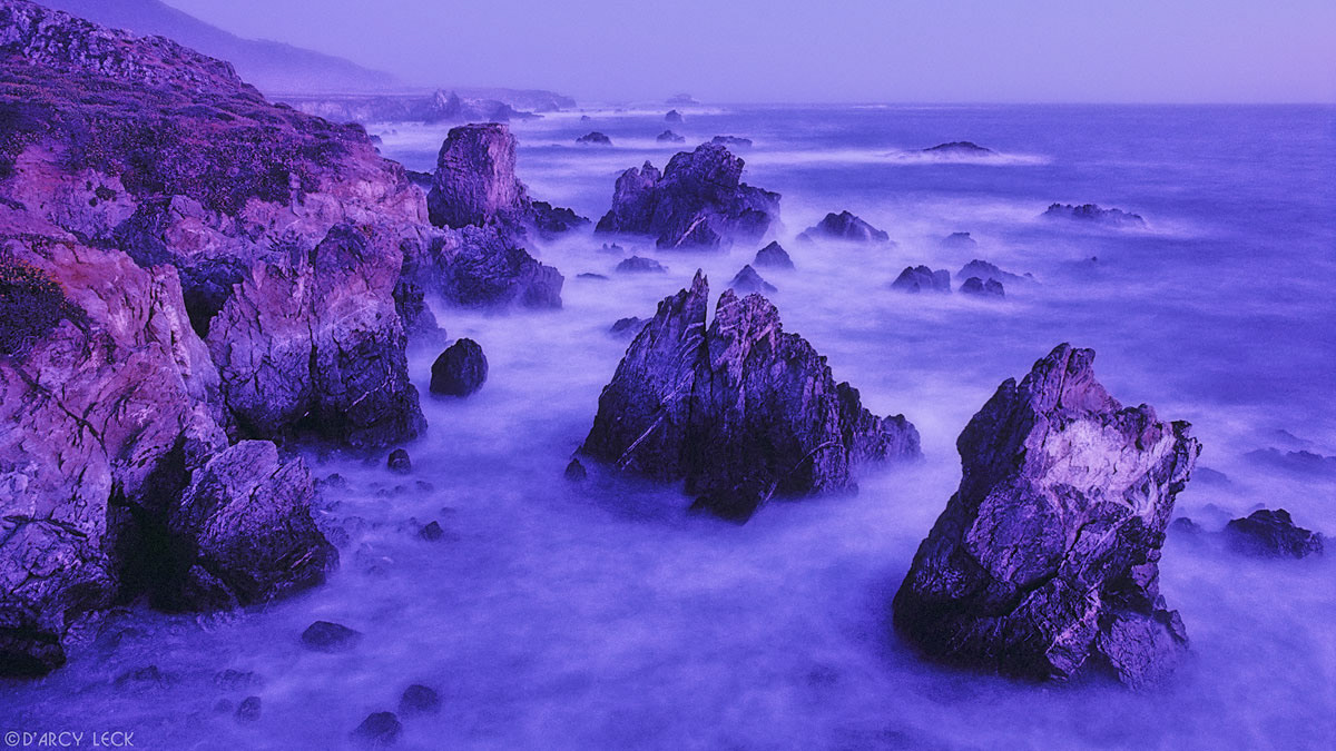 Surf mingles among large rocks at dusk near Lucia, California