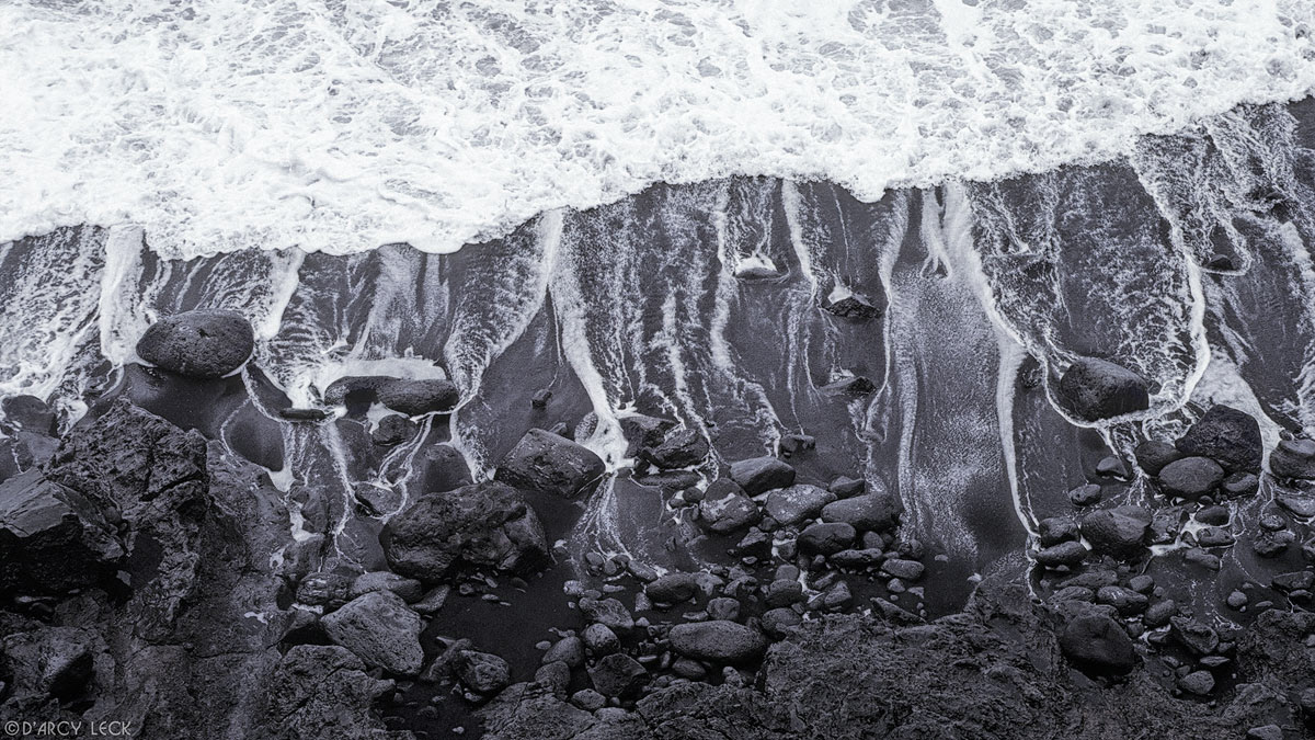 Receding surf leaves trails of water among lava rocks and down black sand beach, big island of Hawaii