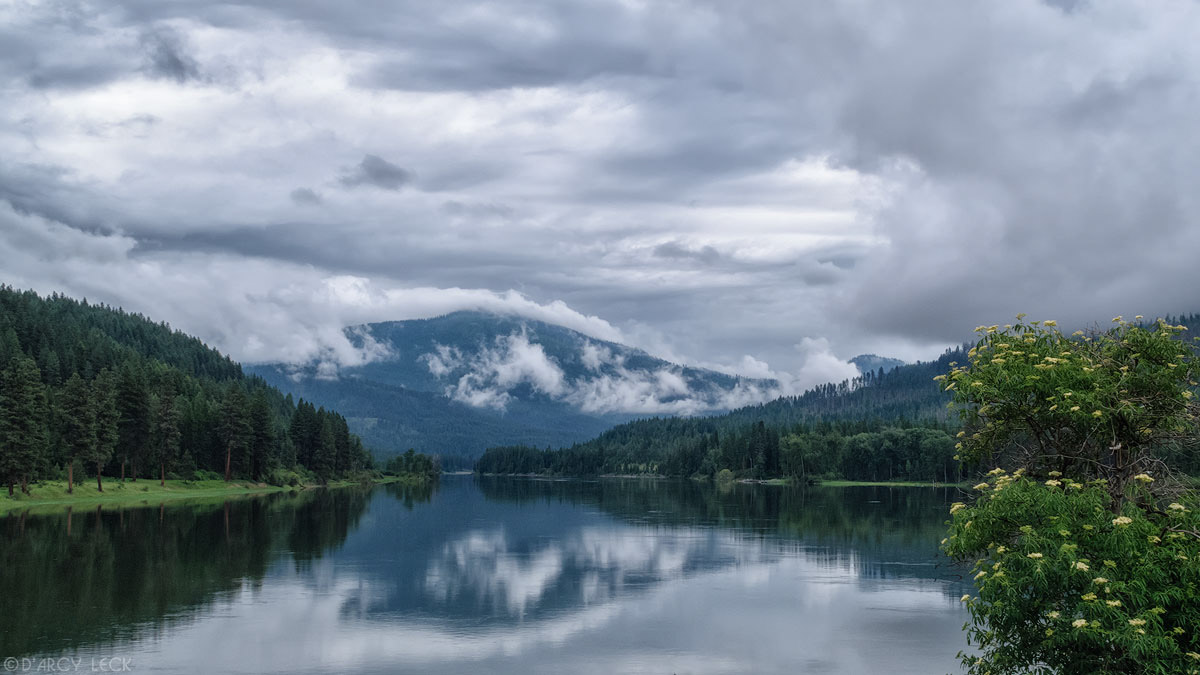 A placid Pend Oreille River reflects cloud enshrouded Selkirk Mountains, Washington