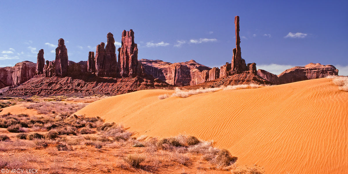 Totem Pole and other sandstone formations rise beyond small sand dunes in Monument Valley, Arizona