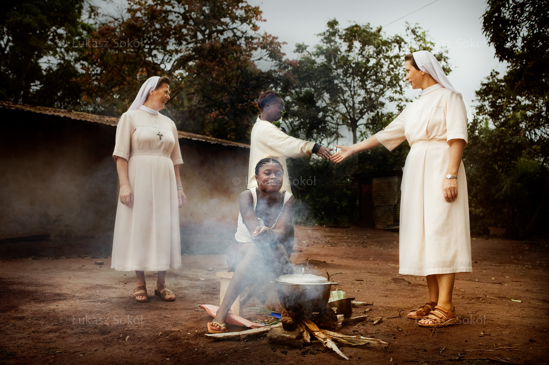 Siostry Celestyna i Danuta ze Zgromadzenia Sióstr Opatrzności Bożej przyglądają się jak Sandrin (16 lat, stoi) i Denis (15 lat) z Ayos gotują obiad. Dziewczynki są objęte programem adopcji serca MAITRI i uczęszczają do szkoły życia.  Ayos to miasto łączące centrum i wschód Kamerunu, drugie pod względem zachorowań na AIDS. Na ulicach pracują dziewczynki od 13 roku życia, wiele z nich chodzi do szkoły. Ayos, Kamerun, 2009