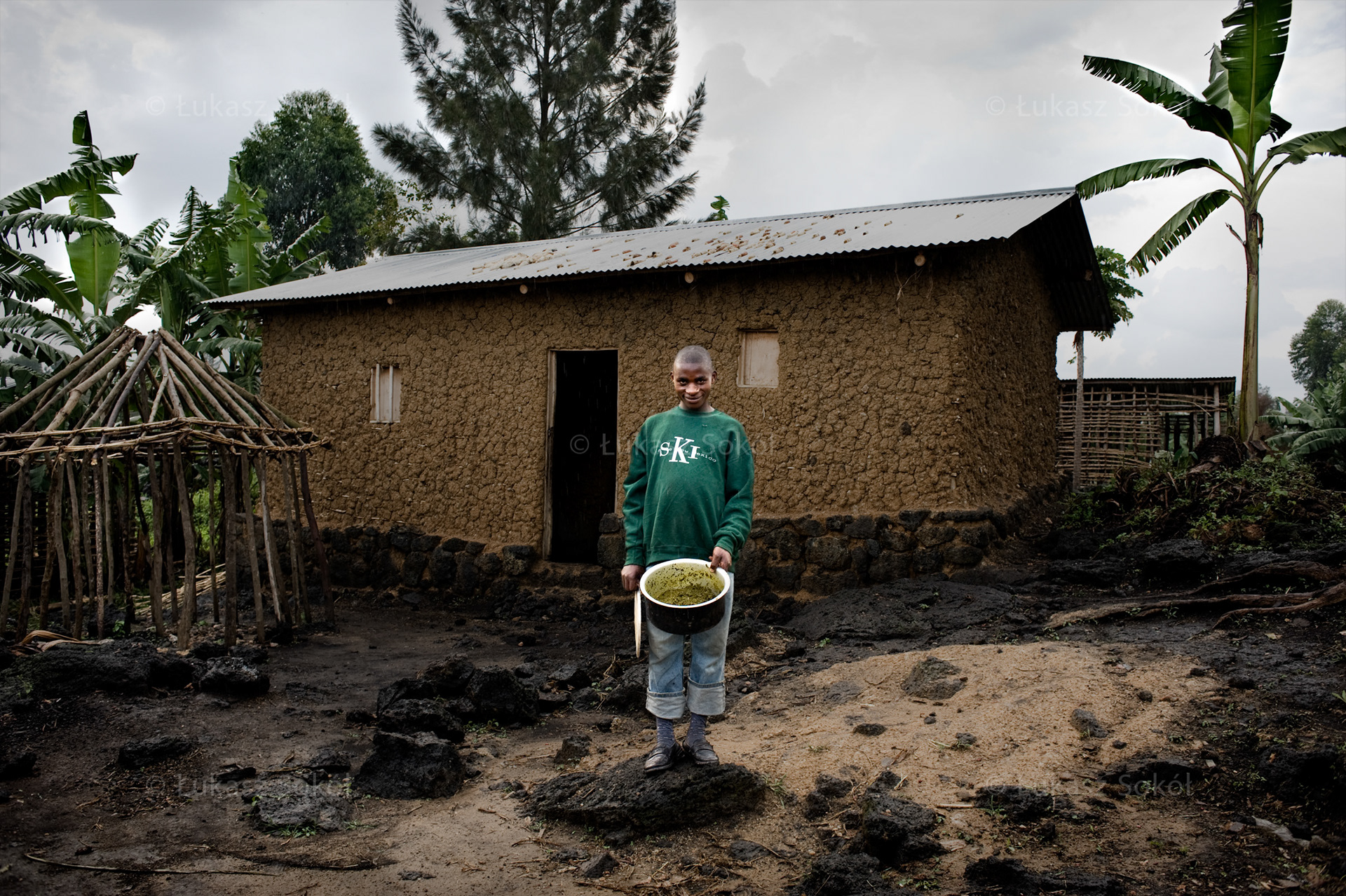 Sebishimbo Sibomana, aged 15, in the 1st year of secondary school. His parents are dead. His mother died 5 years ago, his father – much earlier, he does not even remember him. He lives only with a handicapped brother, who is 10. After school he works in the field rented from a Katale coffee factory and grows beans. He got the pot last Christmas from the distribution to orphans carried out by the Sisters. Without the pot he would not be able to prepare food for himself. He usually has beans or cooks bananas (plantains). He wants to be a nurse. He dreams of peace. The house where he lives was built within the framework of the Maitri project, realized by the Sisters. It cost $400. Their house was very old and it collapsed during a gale. Ntamugenga, DR Congo, 2010