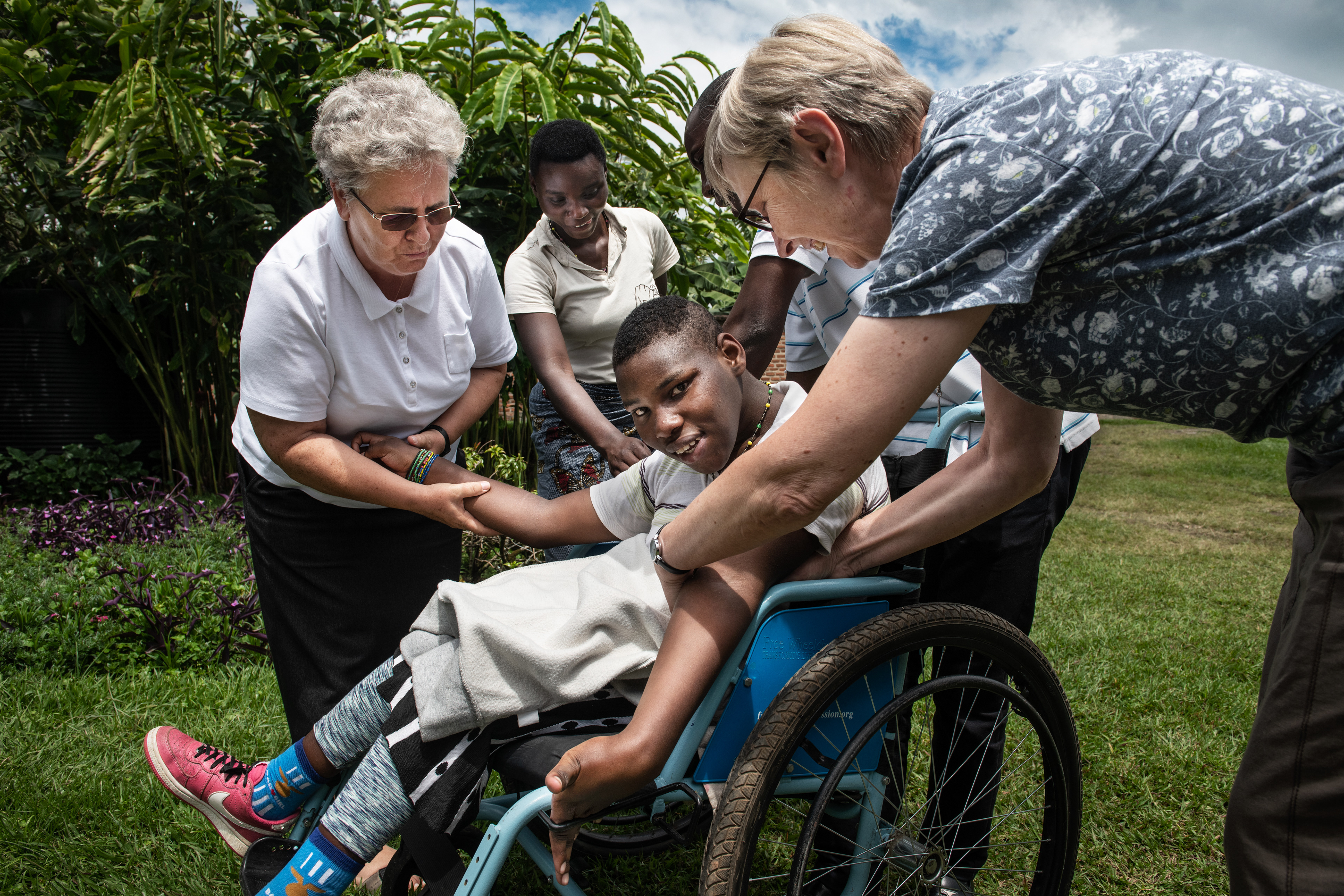 Josiane (13 years old) and Polish missionaries, Sisters of Angels, Alicja and Elizabeth.  Josiane has epilepsy, she cannot walk. She sits in a wheelchair or in her bed.  She is very happy when her sister pushes her wheelchair while running. The sisters try on a special belt that they sewed for Josiane in their sewing workshop. Thanks to it, she will not fall out of the wheelchair during her next epileptic seizures.  Over 80% of Rwandans live in rural areas. Most of them cannot afford health insurance, they have limited access to medical care. This particularly affects people with disabilities.  In Nyakinama, Polish missionary Sisters of Angels provide medicines, food, wheelchairs and equipment to improve their lives, and finance necessary treatments and surgeries. Rwanda 2019