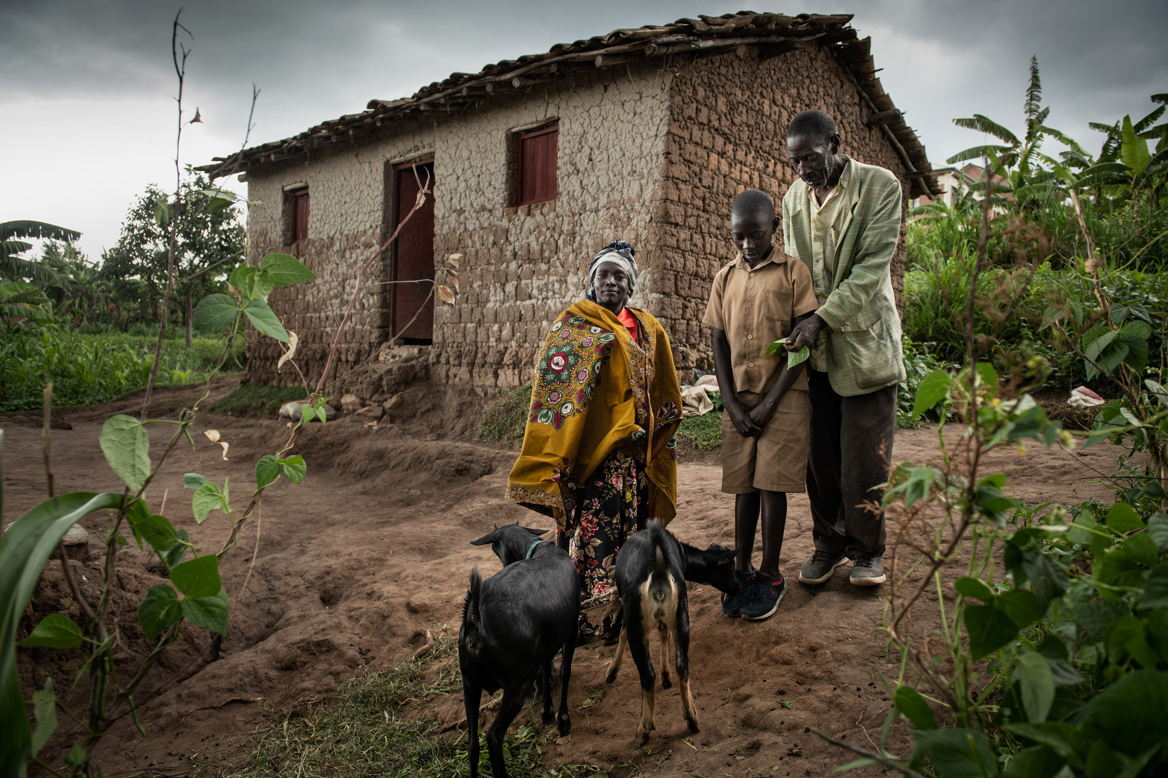 A family in front of a house that they rent for 3,000 fr per month (1,85 Euro). In exchange for working in the field, they get a piece of land for their own use. They have no income, only money from aid. But they are resourceful, they save money and buy pigs and goats with it. They go around the area looking for food for the animals. They buy pigs for 15,000 fr (9 Euro)  and sell them for 30,000 fr (18 Euro)  after 5 months. When the goats reproduce, they sell the little ones. Kabgayi, Rwanda 2021