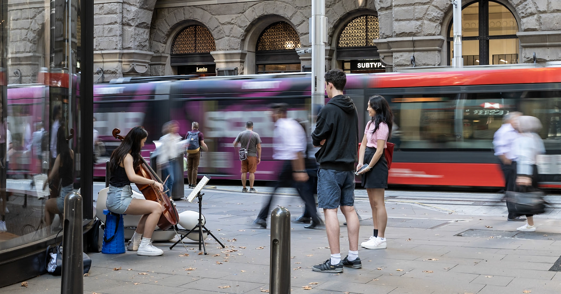 A cello player near Martin Place lets a passerby have a go.
