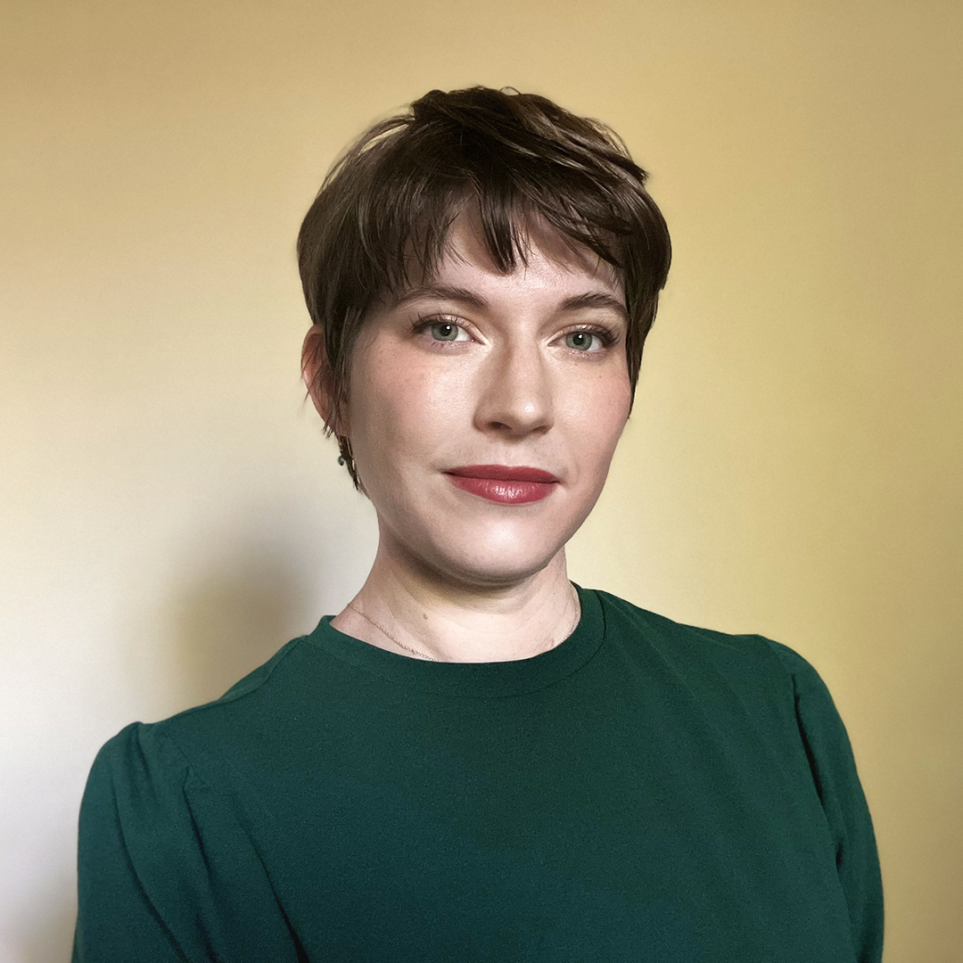 Photo of Amanda looking at the camera in a dark green shirt on an off-white background.