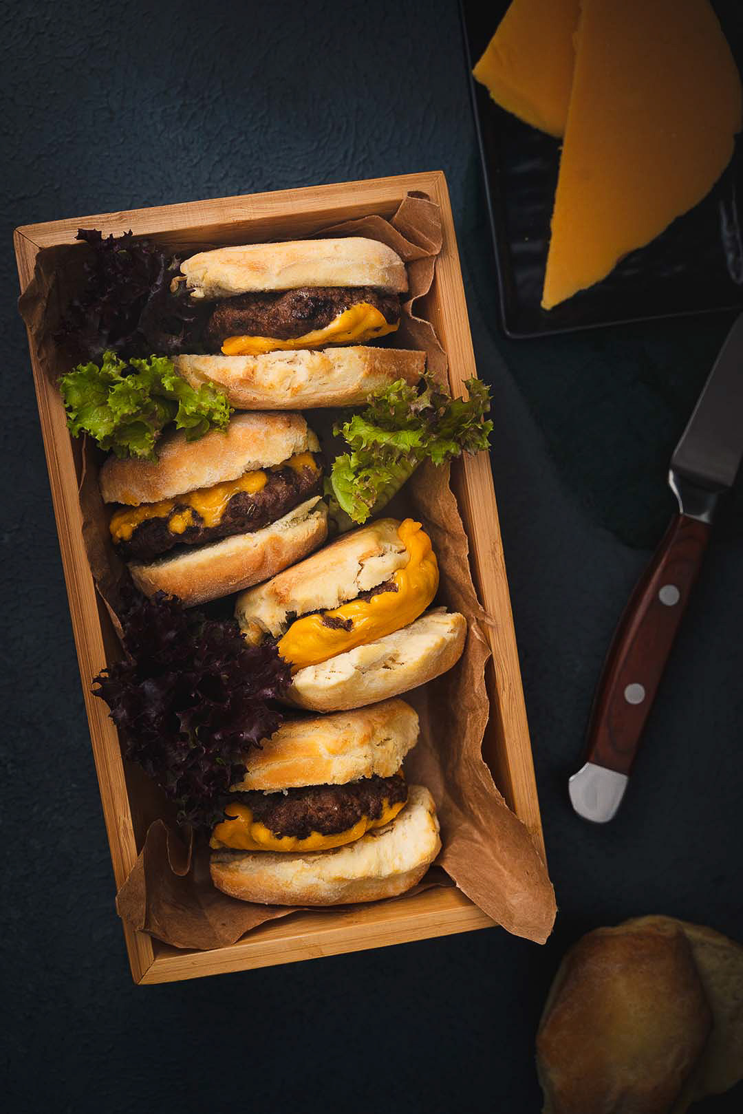 Biscuit Cheeseburger: Rustic Charm in a Wooden Basket - Captured in a moody, dark setting, this innovative photograph showcases a mouthwatering cheeseburger sandwiched between biscuit buns and neatly arranged in a wooden basket. Its unique twist on a classic favorite is both visually appealing and irresistibly delicious. in a Basket with Lettuce - A basket of homemade cheeseburgers, perfectly grilled with melted cheese and fresh lettuce, ready for a satisfying meal. This simple yet delicious dish is perfect for a family dinner or casual gathering.