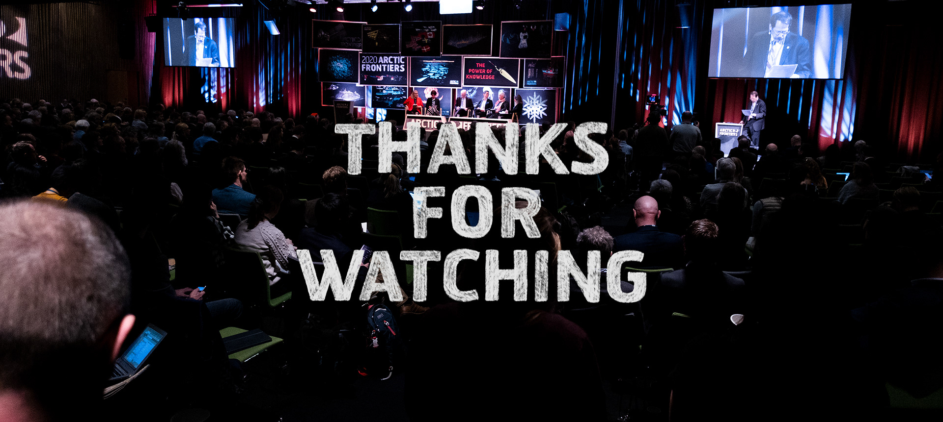 Photo of stage with panel and audience from distance with chalk typography saying "Thanks for watching".