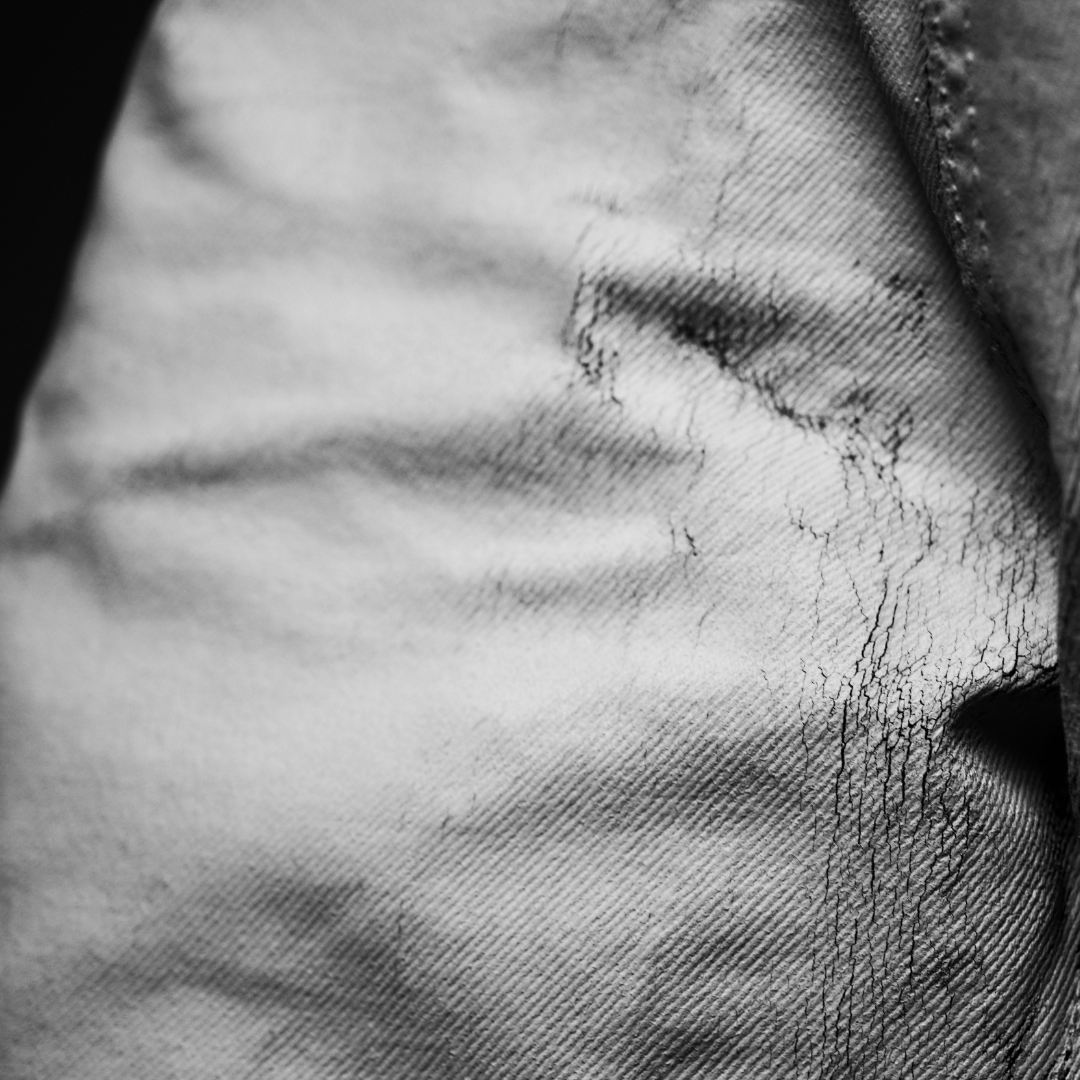 Extreme close-up macro black and white photograph of cracking white Bianchetto paint on denim fabric, Margiela philosophy, movement and wear, MINUSELEVEN AUDIOVISUAL