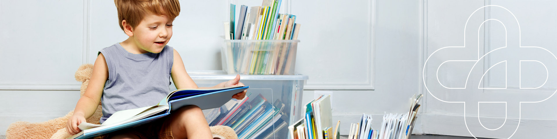 Junge sitzt auf einem Plüschsessel und liest in einem aufgeschlagenen Buch, umgeben von vielen weiteren Büchern in transparenten Boxen – Symbolbild für Lerntherapie in der Ergotherapie.