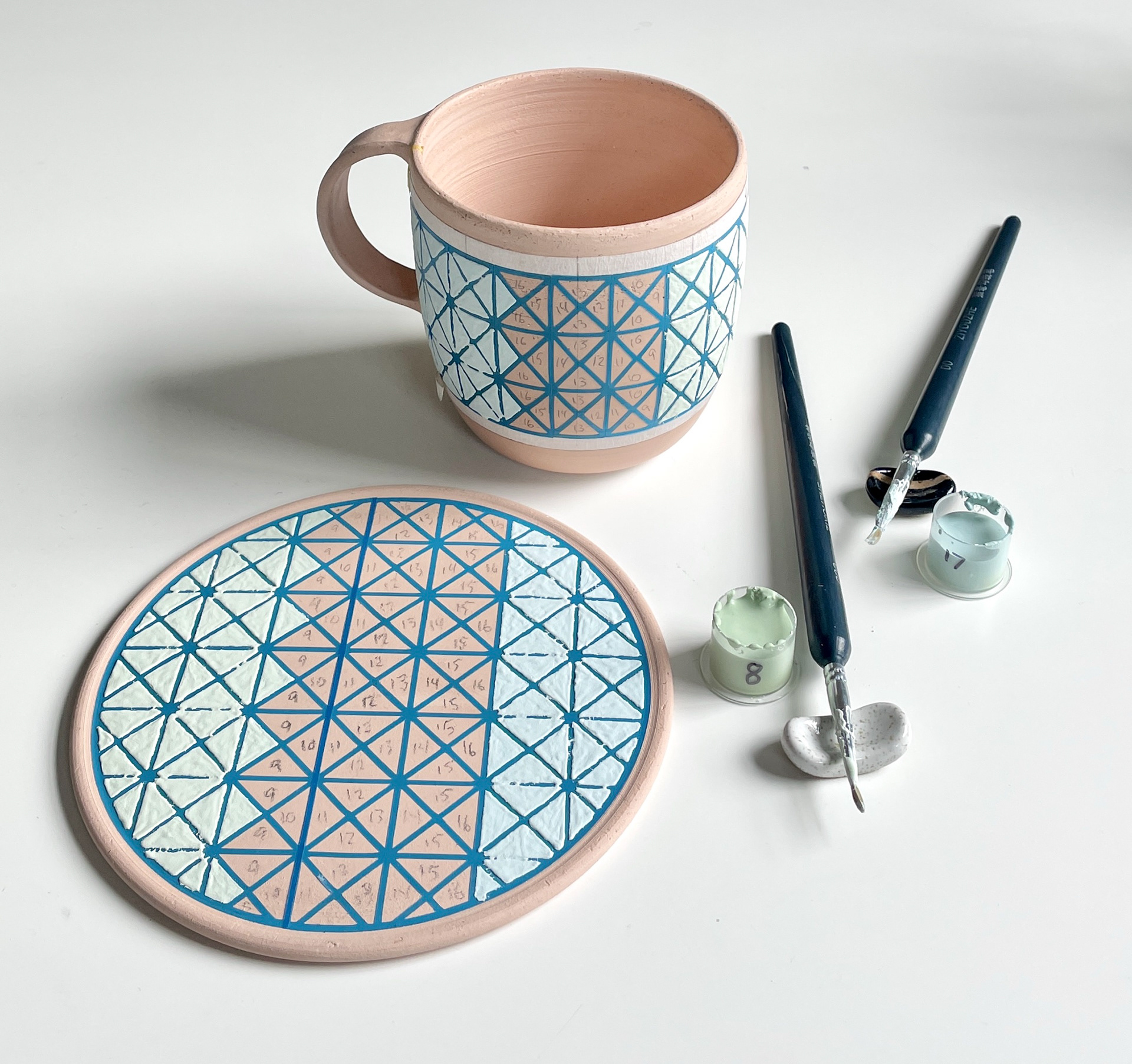 Vinyl being used as a stencil to glaze a stoneware mug and wall tile