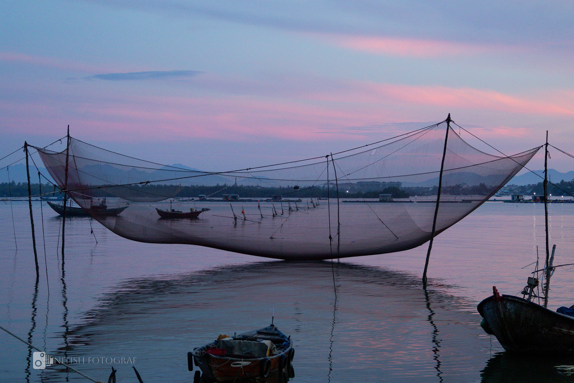 Boats resting in still waters as the sky awakens with soft pastel hues