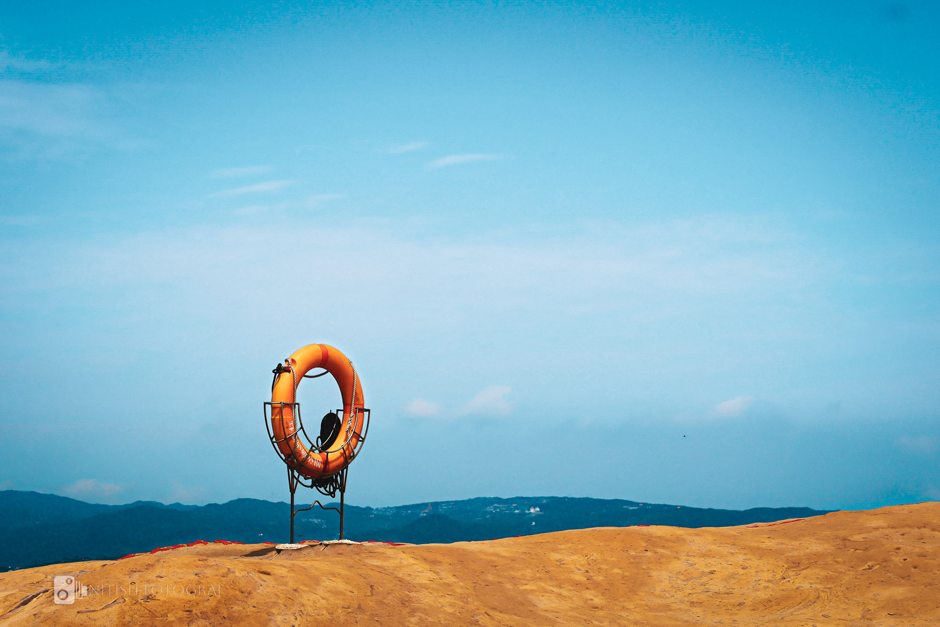 A vibrant lifebuoy against a panoramic coastal view, where land meets the sea