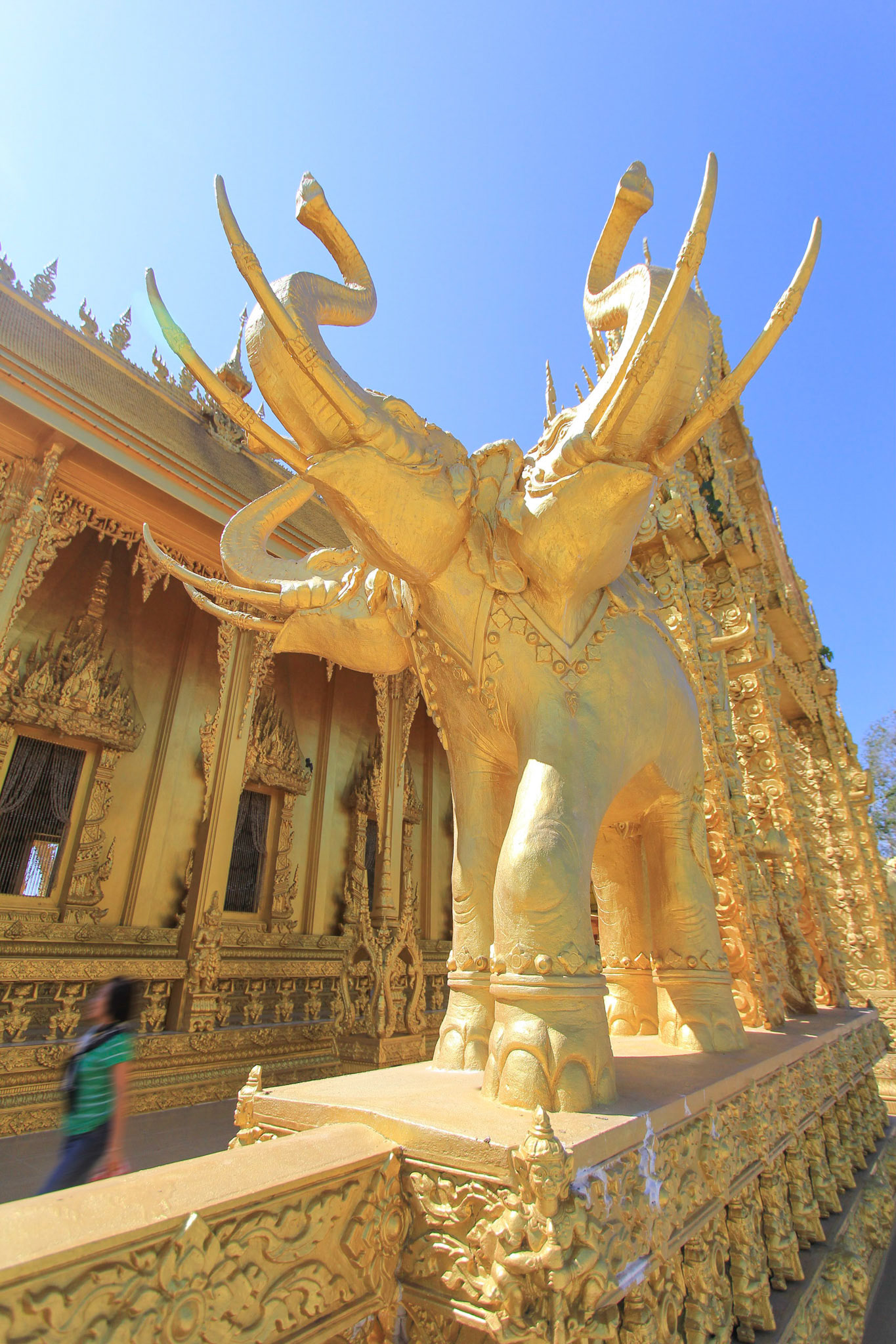 Golden three head elephant statue in front of golden buddhist temple in Chachoengsao, Thailand on the sunshine day. Focused on elephant statue.