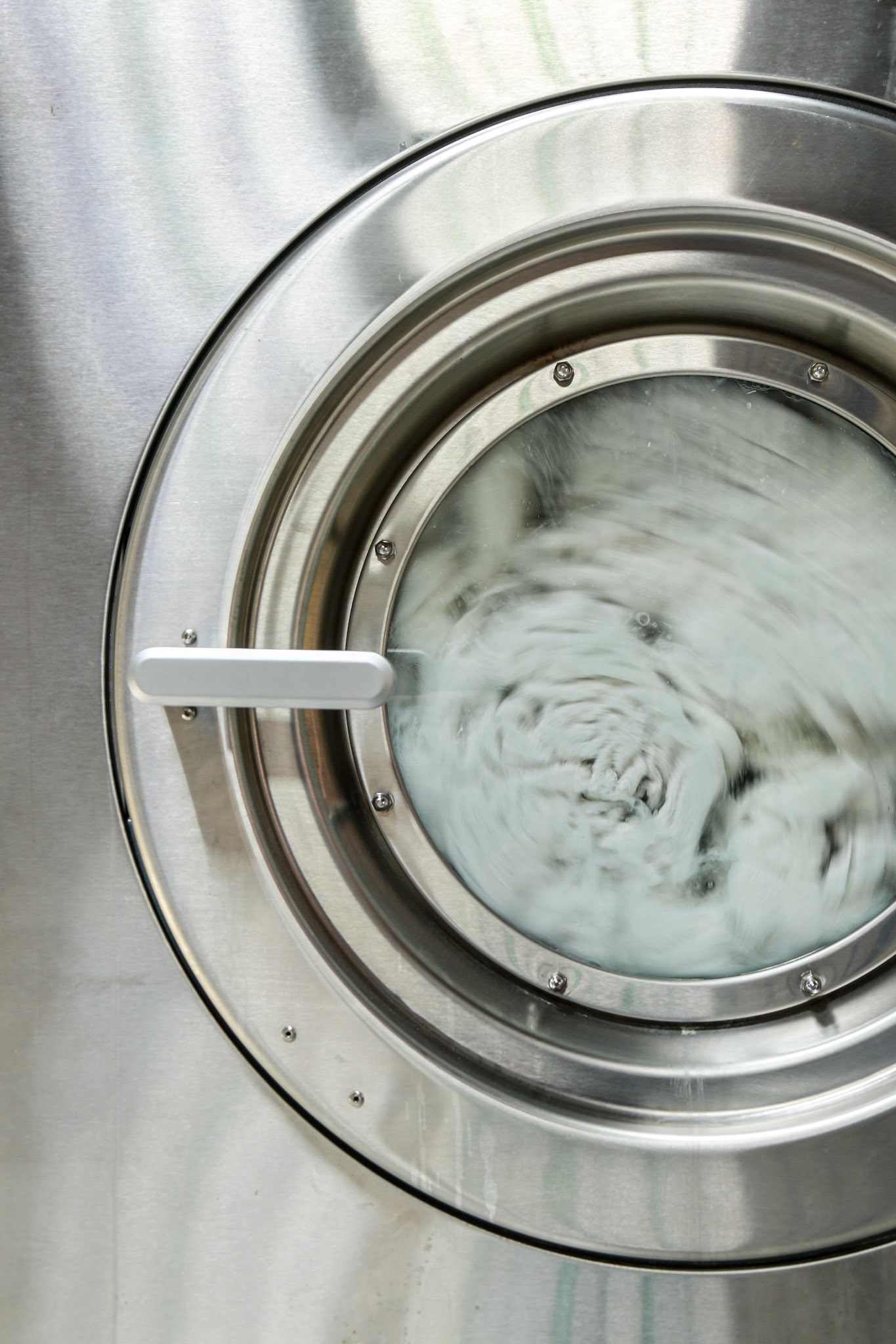 Towels are spinning inside the front door of stainless steel industrial washing machine. Shot taken in the factory.