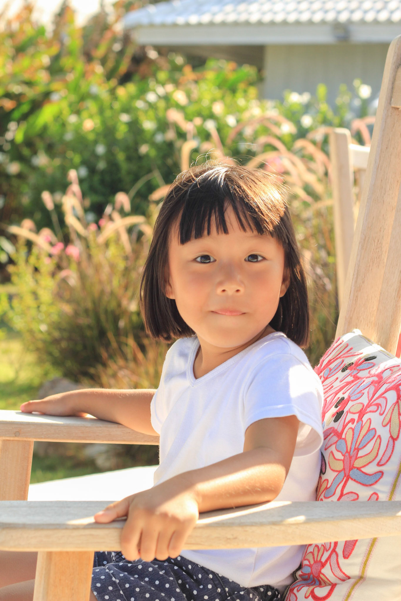 A girl is sitting on the wooden chair surprisingly looking with the garden background. Focus on her face.