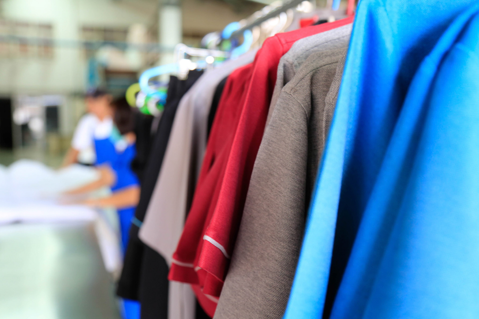 Clean uniforms are hanging on clothes line ready for delivery. Off focus staffs are over the background. Shot taken in the factory.