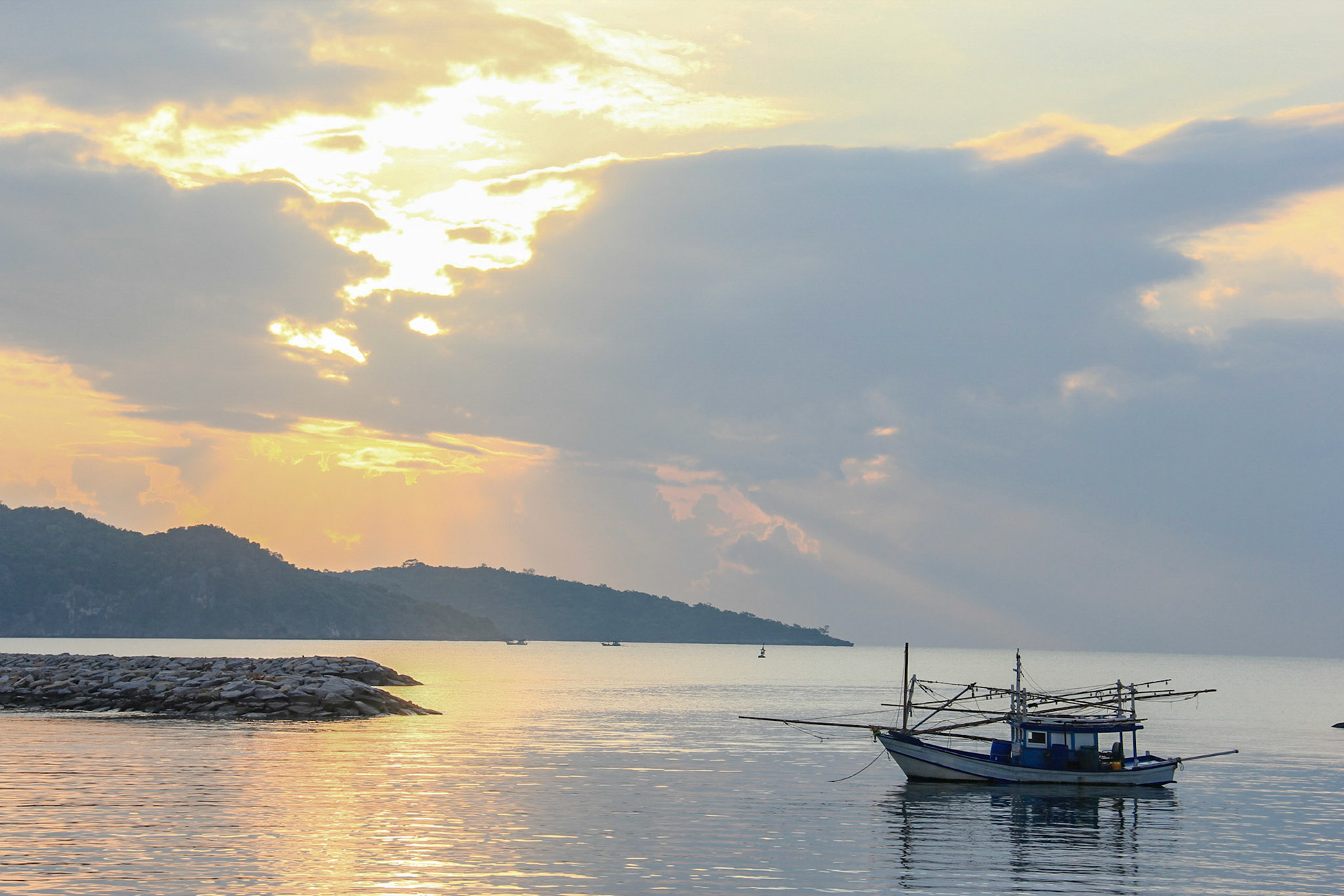 A fishing boat lies in the sea at sunset with island in the background.