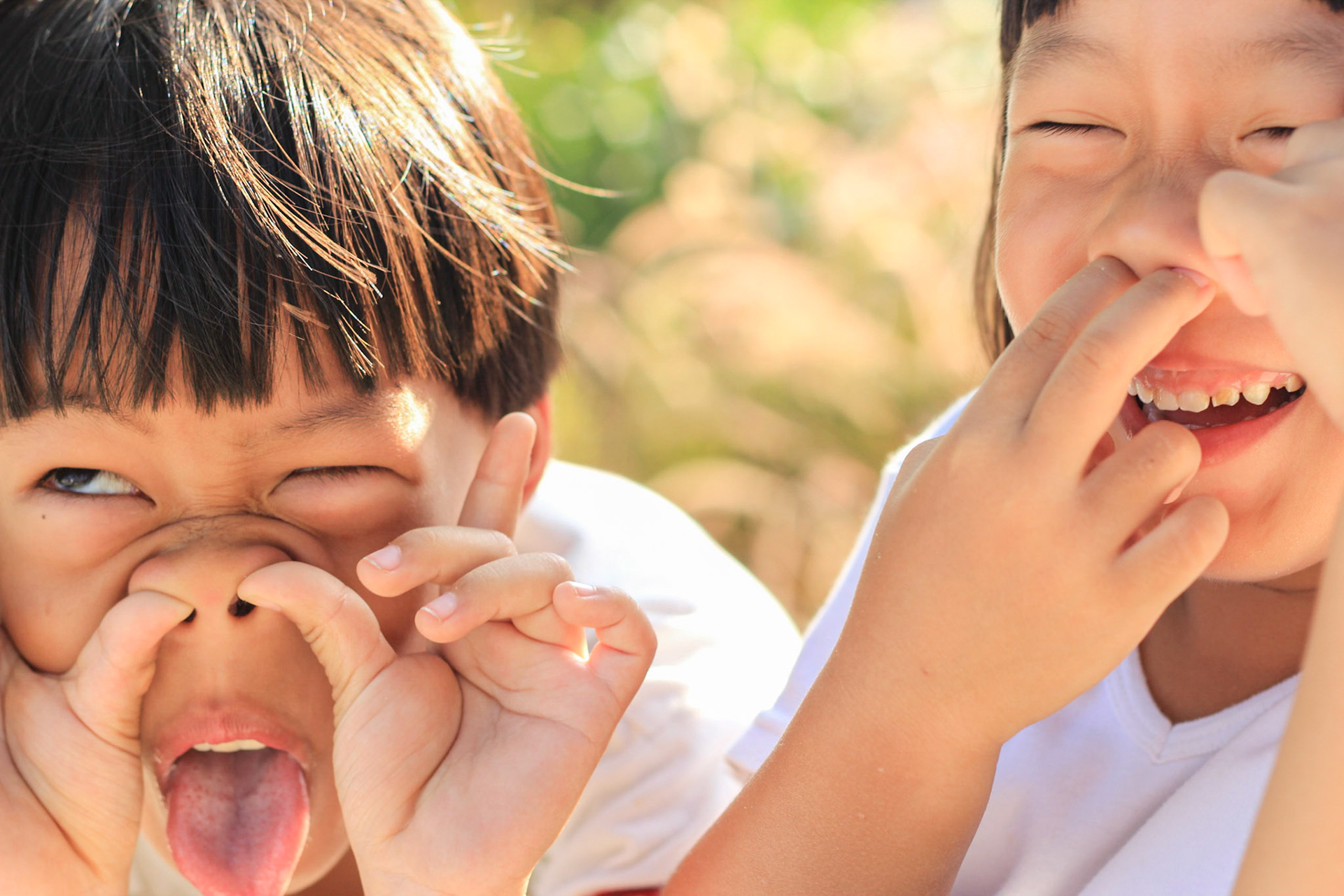Two children, boy and girl are laughing and making fun with the garden background. Close up shot.