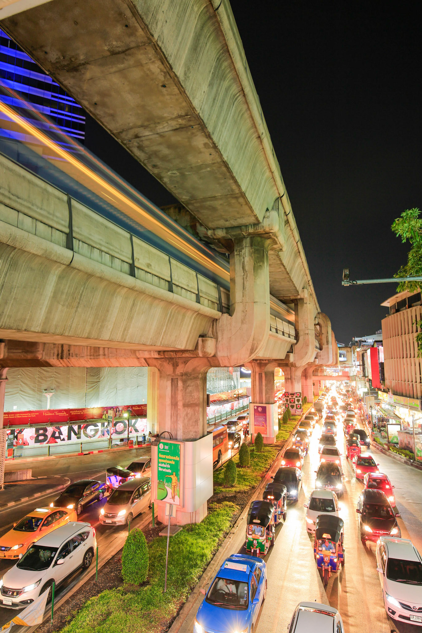 BANGKOK THAILAND - Twilight Bangkok with moving skytrain above car traffic and street lights.
