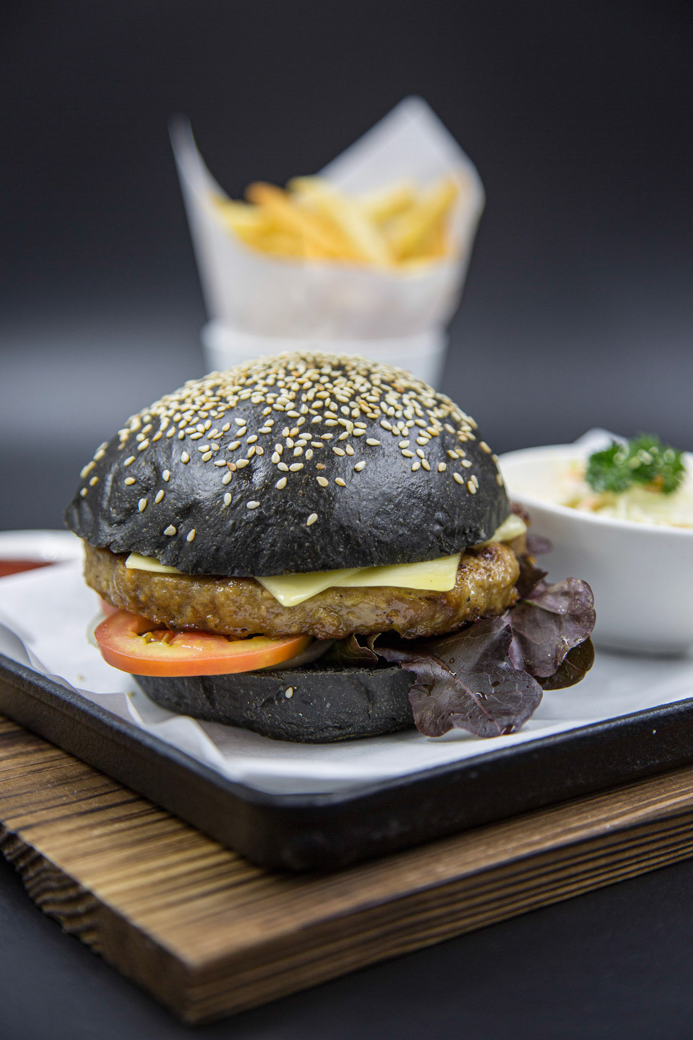 Charcoal beef burger set served with french fries and coleslaw on the wooden tray with dark background. Focused on cheese, beef and vegetables.