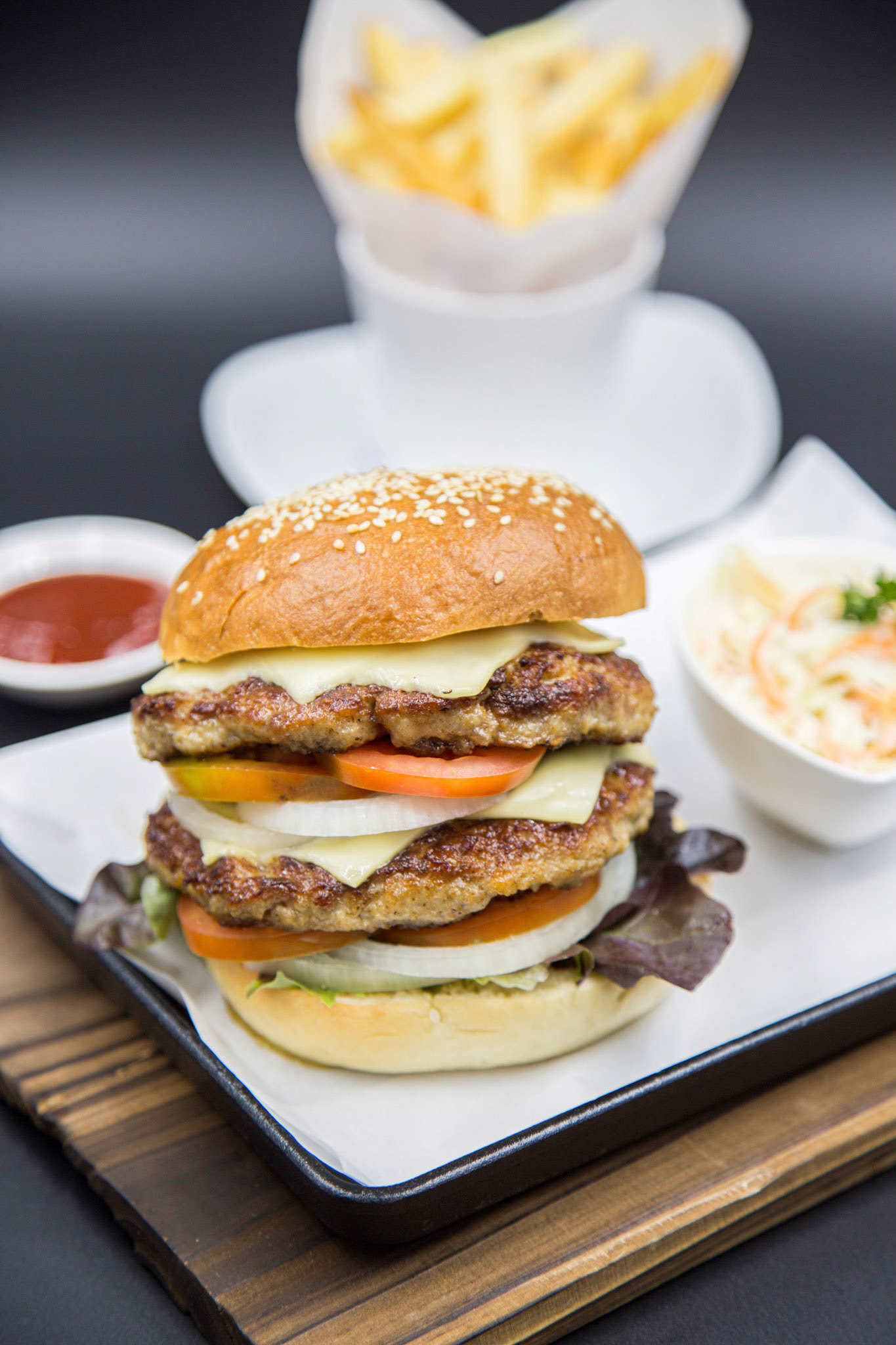 Double cheese burger set served with french fries and coleslaw on the wooden tray with dark background. Focused on  cheese, beef and vegetables.