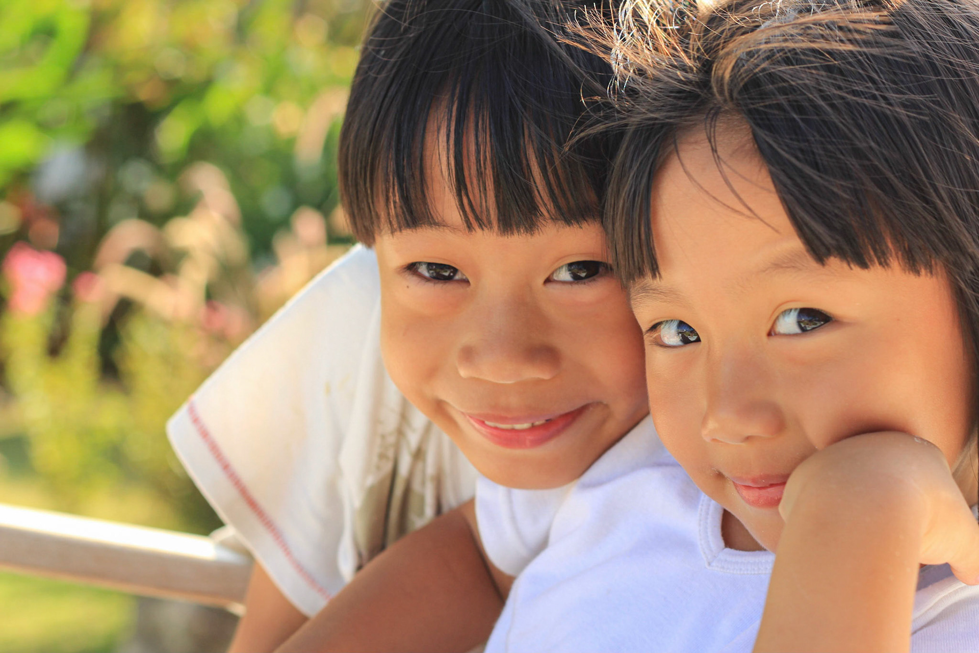 Two children, boy and girl sit together with the garden background. Close up shot.