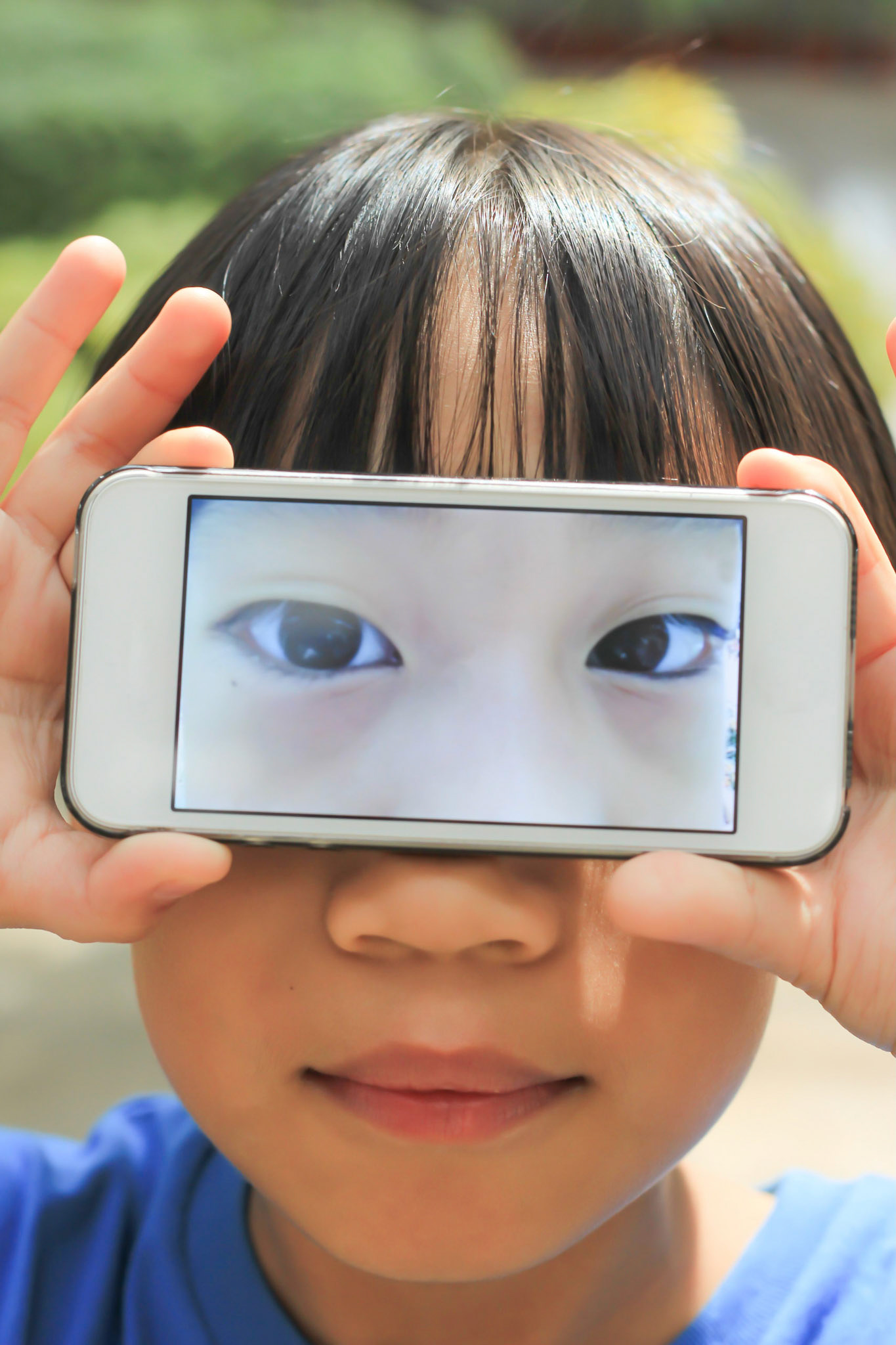 Asian boy is making fun by placing a smartphone as his eyes on the face. Close up shot.