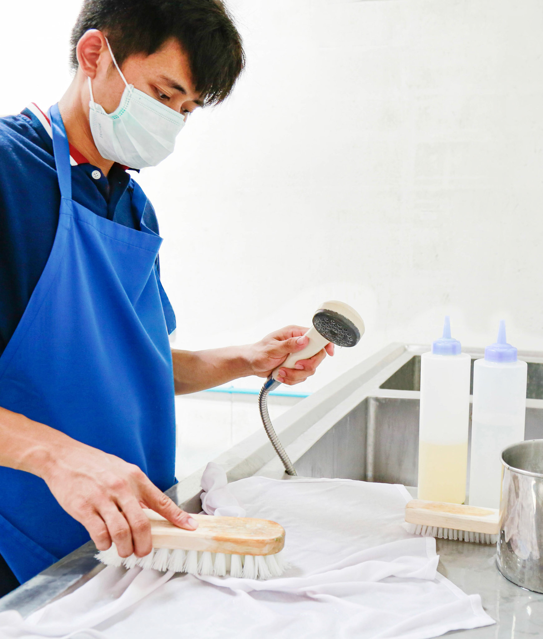 A laundry staff is holding a shower head, brushing a napkin in process of stain removal spotting chemicals. Shot taken in the factory.