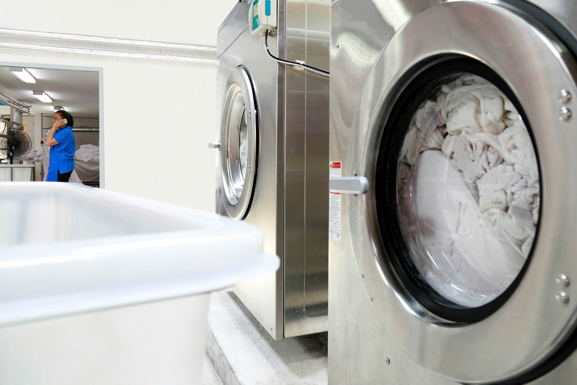 Industrial washing machine are spinning while a laundry staff is talking on the phone over the background. Shot taken in the factory.