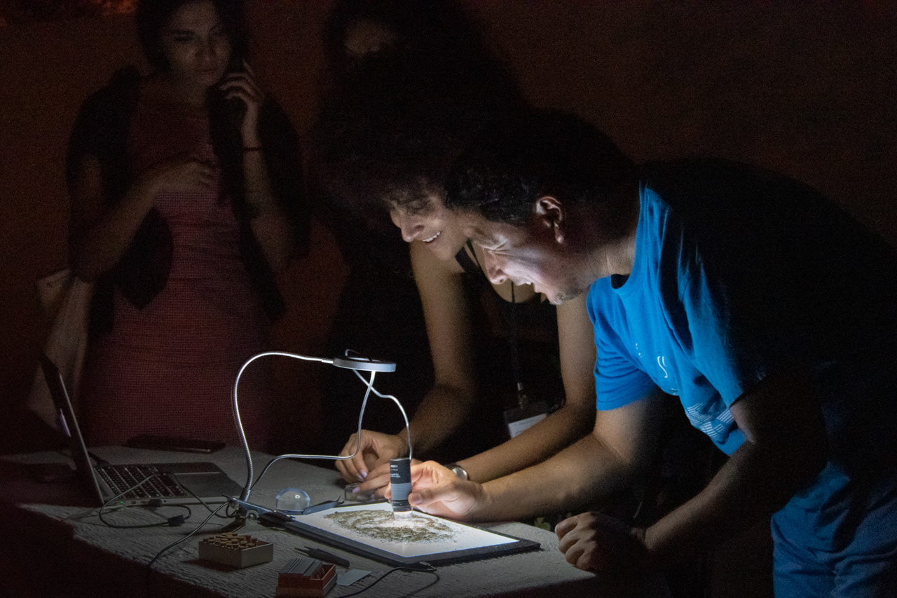 A microscope camera controlled by the viewer focuses on individual grains of sand from Djerba.