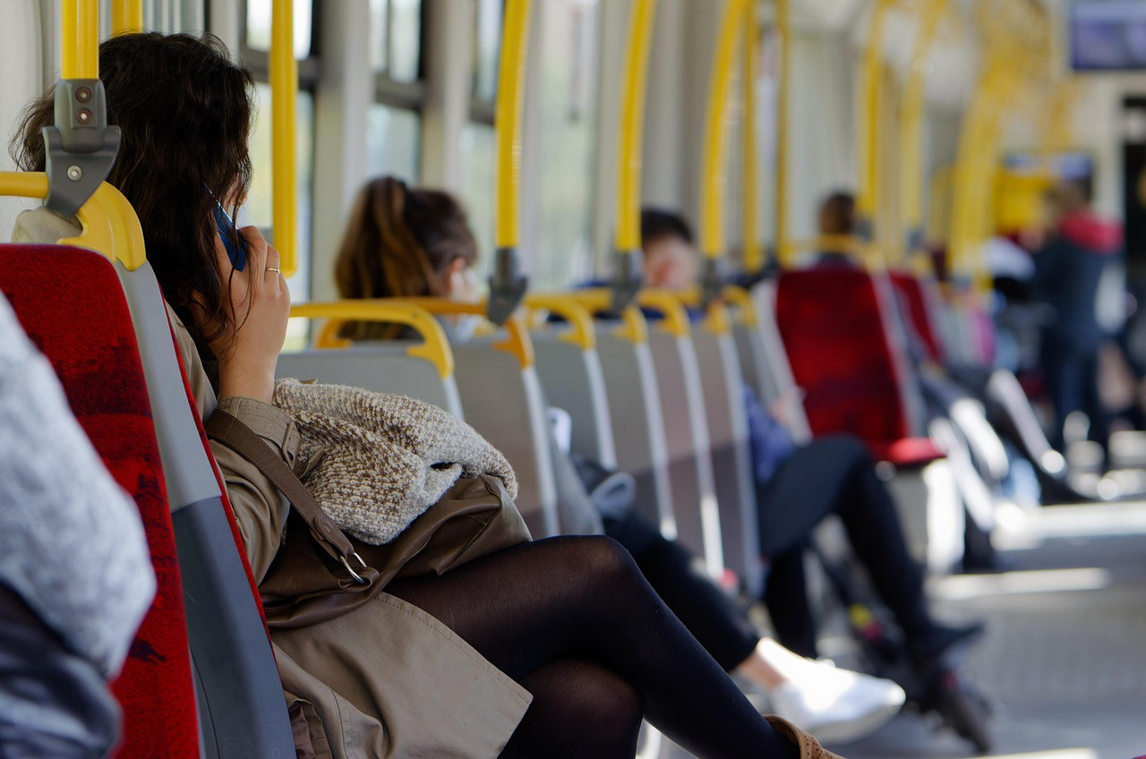 Passengers seated inside a sunlit tram, some using phones.