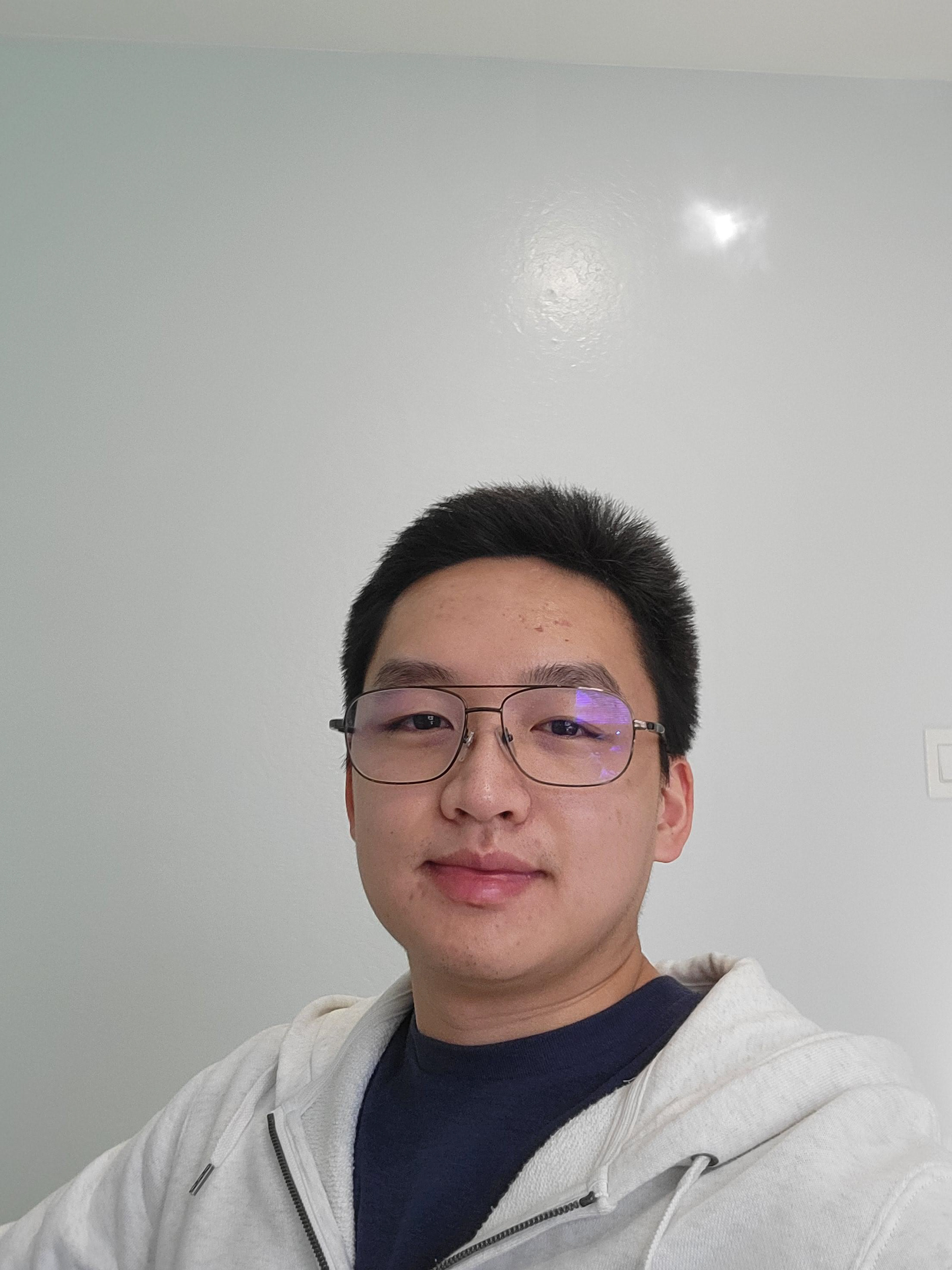 A photo of the artist. Tommy Truong is wearing glasses, a white zip-up hoodie, and a plain navy blue shirt.