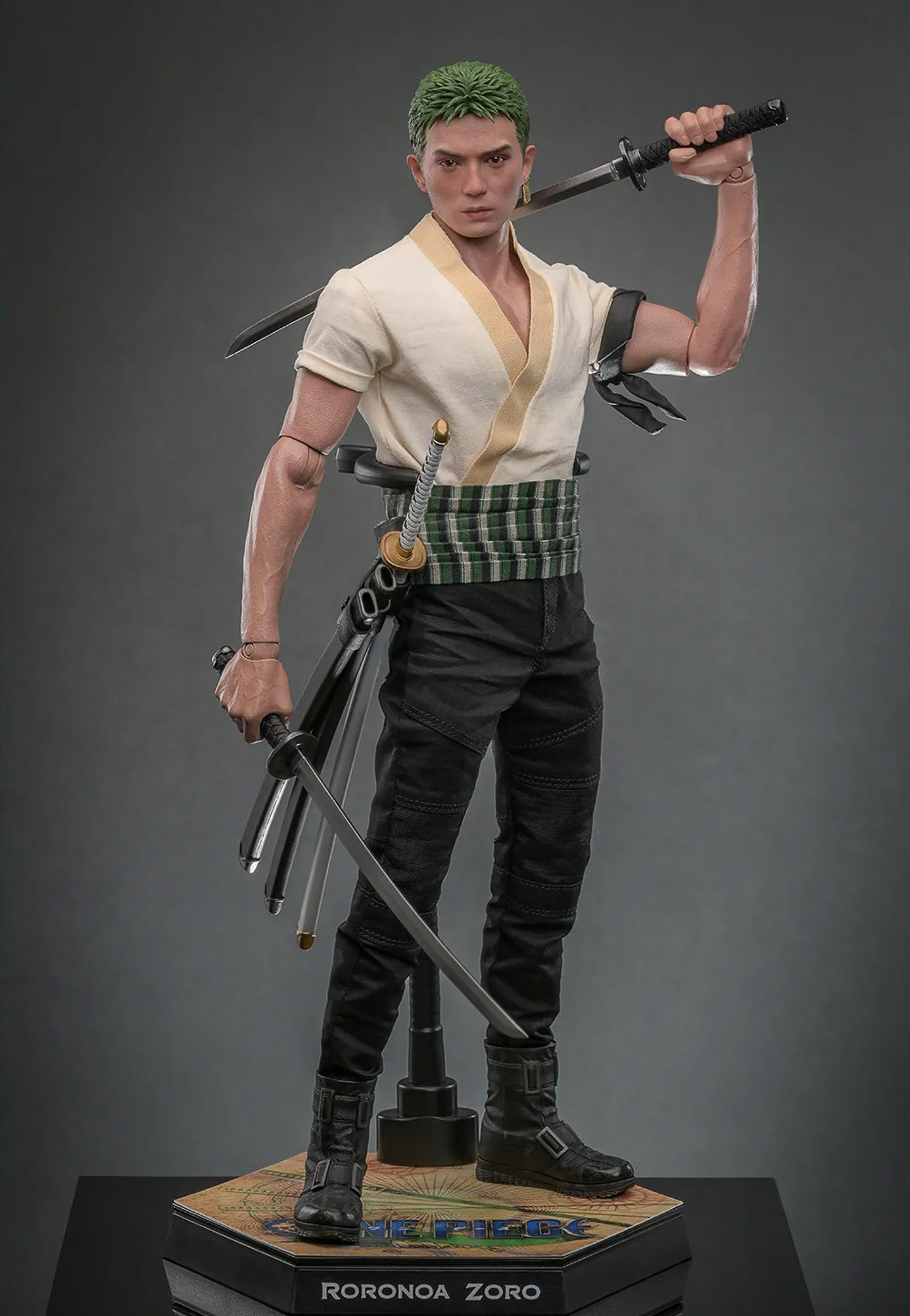 A professional studio photograph of a highly detailed Roronoa Zoro collectible action figure from the Netflix live-action series One Piece. The figure, based on Mackenyu’s portrayal, is shown in a dynamic three-sword style pose, wearing a white short-sleeved shirt, green haramaki sash, and black trousers. It stands on a hexagonal display base featuring a compass map design and the name 'RORONOA ZORO.' The image highlights the photographic precision used to translate on-set unit stills into authentic consumer products.