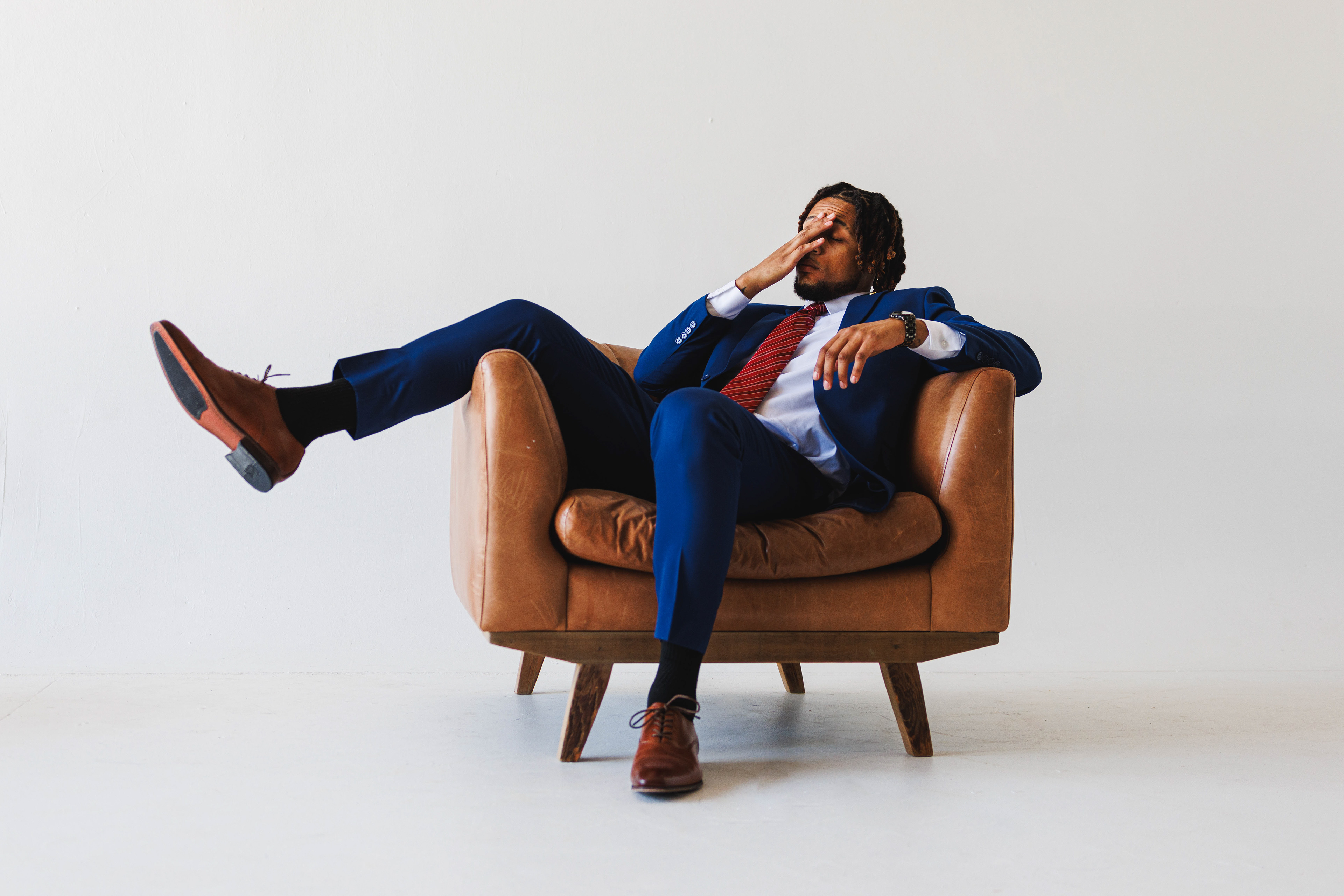 @vastitude | Studio Headshot Photoshoot with a blue suit, brown leather couch, and a drink.