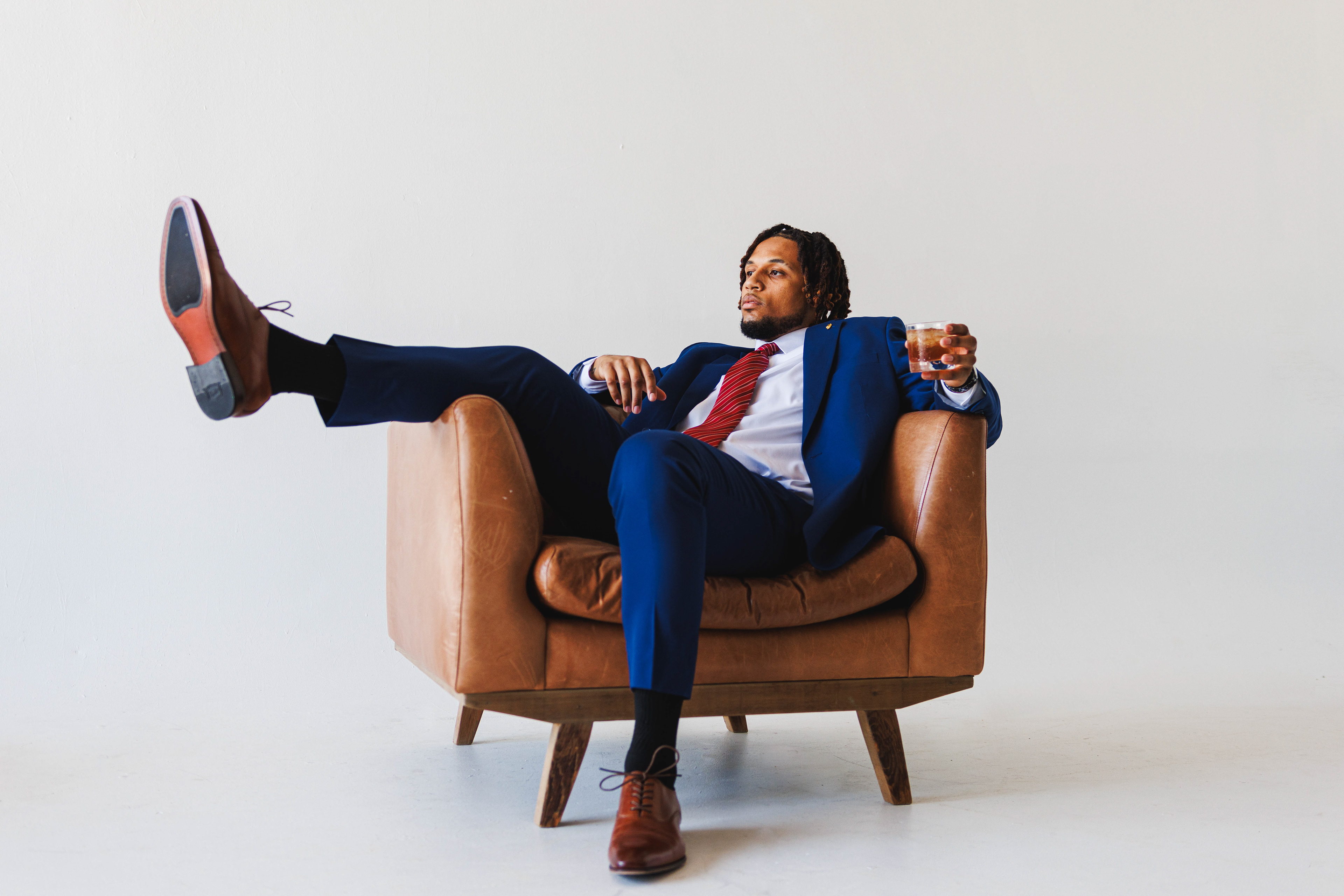@vastitude | Studio Headshot Photoshoot with a blue suit, brown leather couch, and a drink.