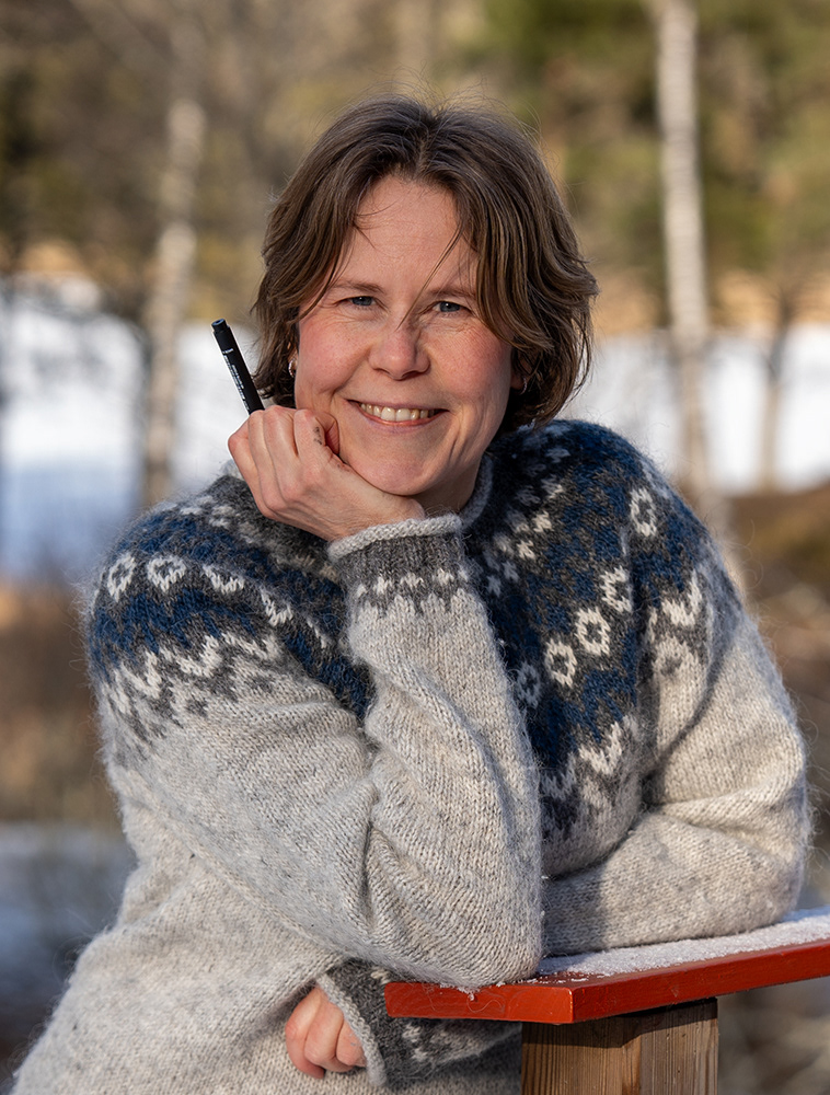 Outdoor portrait of the artist ann-katrin persson with a pen in her hand and in an icelandic lopapeysa sweater