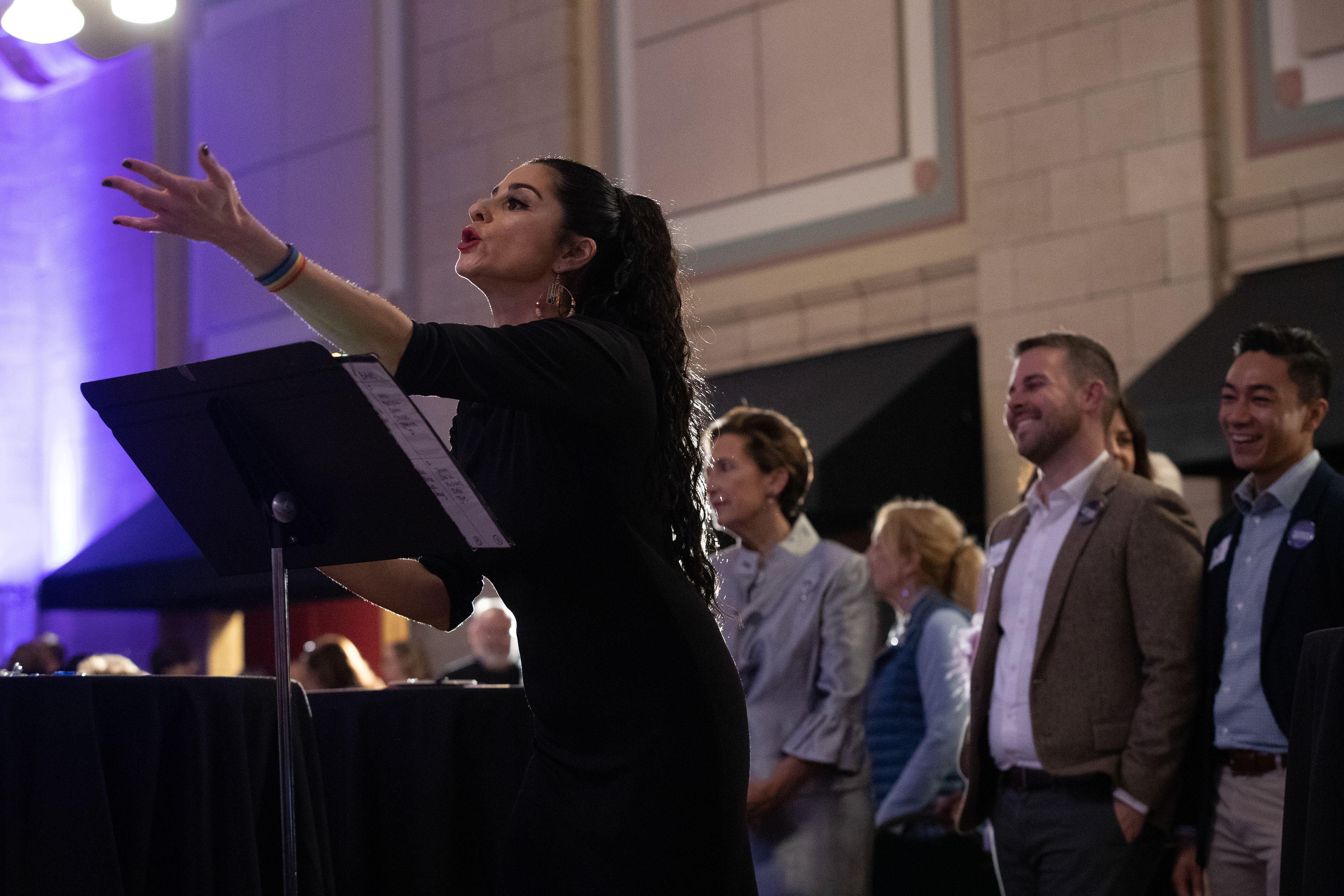 Lincoln Queer Choir Director Juju Tyner leads the choir as they perform during Patty Pansing Brooks' election night party at Lincoln Station Great Hall on Nov. 8, 2022. Patty Pansing Brooks and her son Taylor Brooks and his partner Greg Rafal stand behind her.(Nebraska News Service / Naomi Delkamiller)