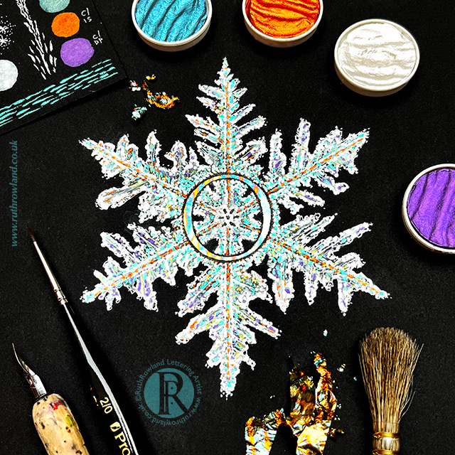 Lettering Artist London UK Ruth Rowland © Photo of gilded snowflake on desktop using colourful variegated metal leaf with pen, brushes and metallic watercolours