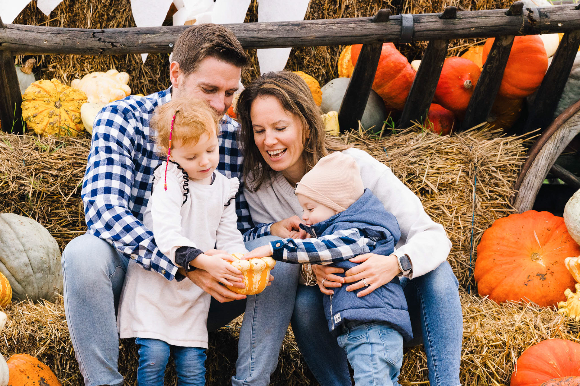 Familienfotografie im Herbst: Eltern mit zwei kleinen Kindern, umgeben von Kürbissen und Herbstfarben